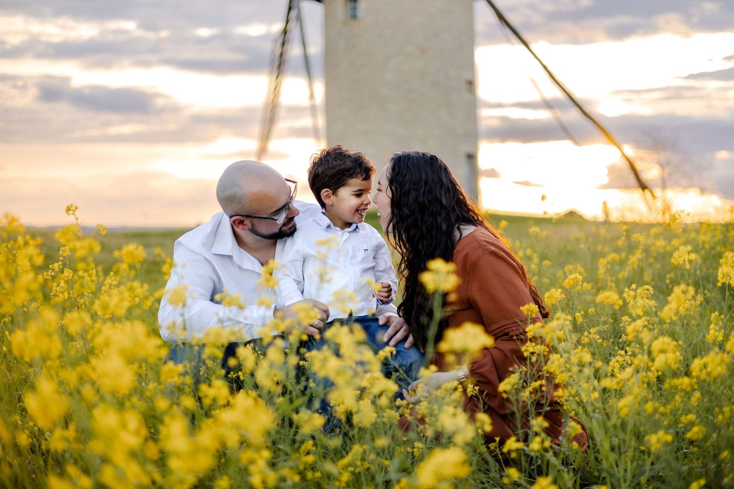 Famille dans un champs de fleurs avec un moulin en fond au coucher du soleil. Séance photo grossesse en extérieur à Langon, Sud Gironde