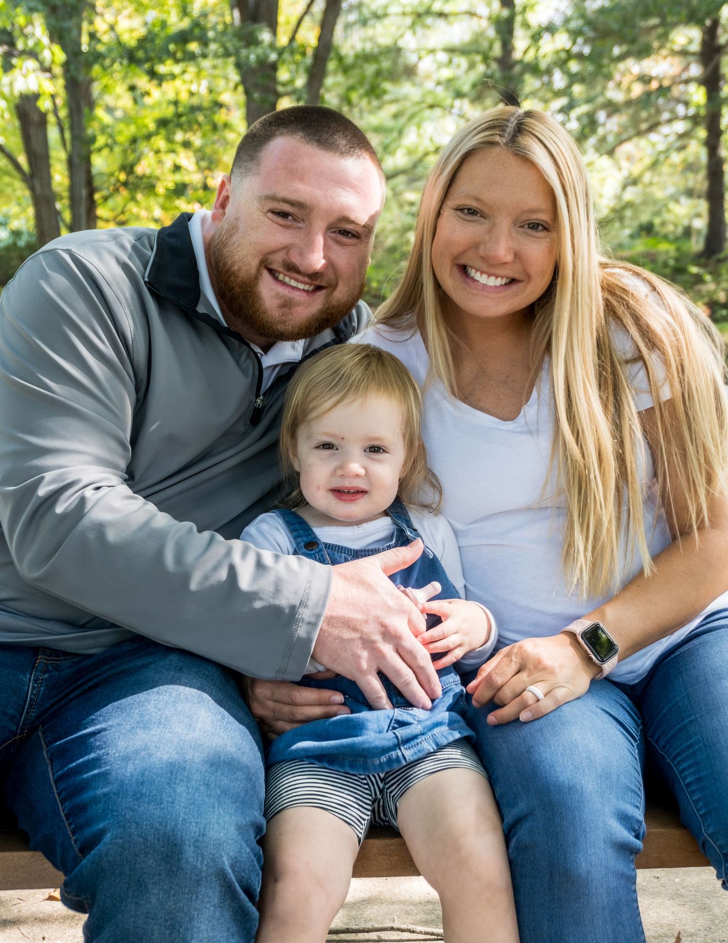 A young family sits close together on outdoor steps, sharing intimate moments and smiles.