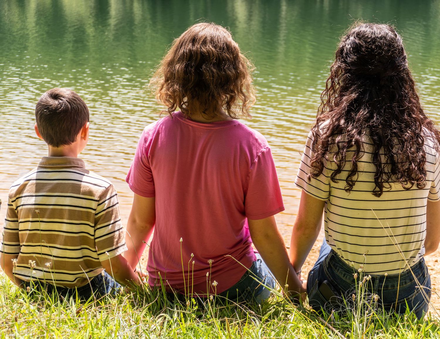 Group sitting together by a peaceful green lake on a sunny day.