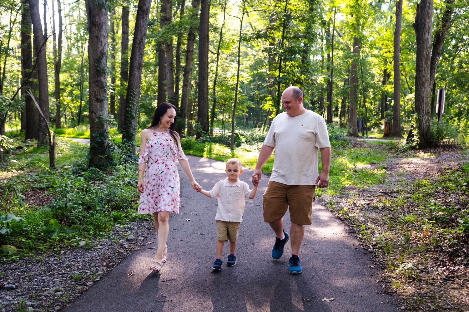 Family walking together on a tree-lined nature trail during a sunny afternoon.
