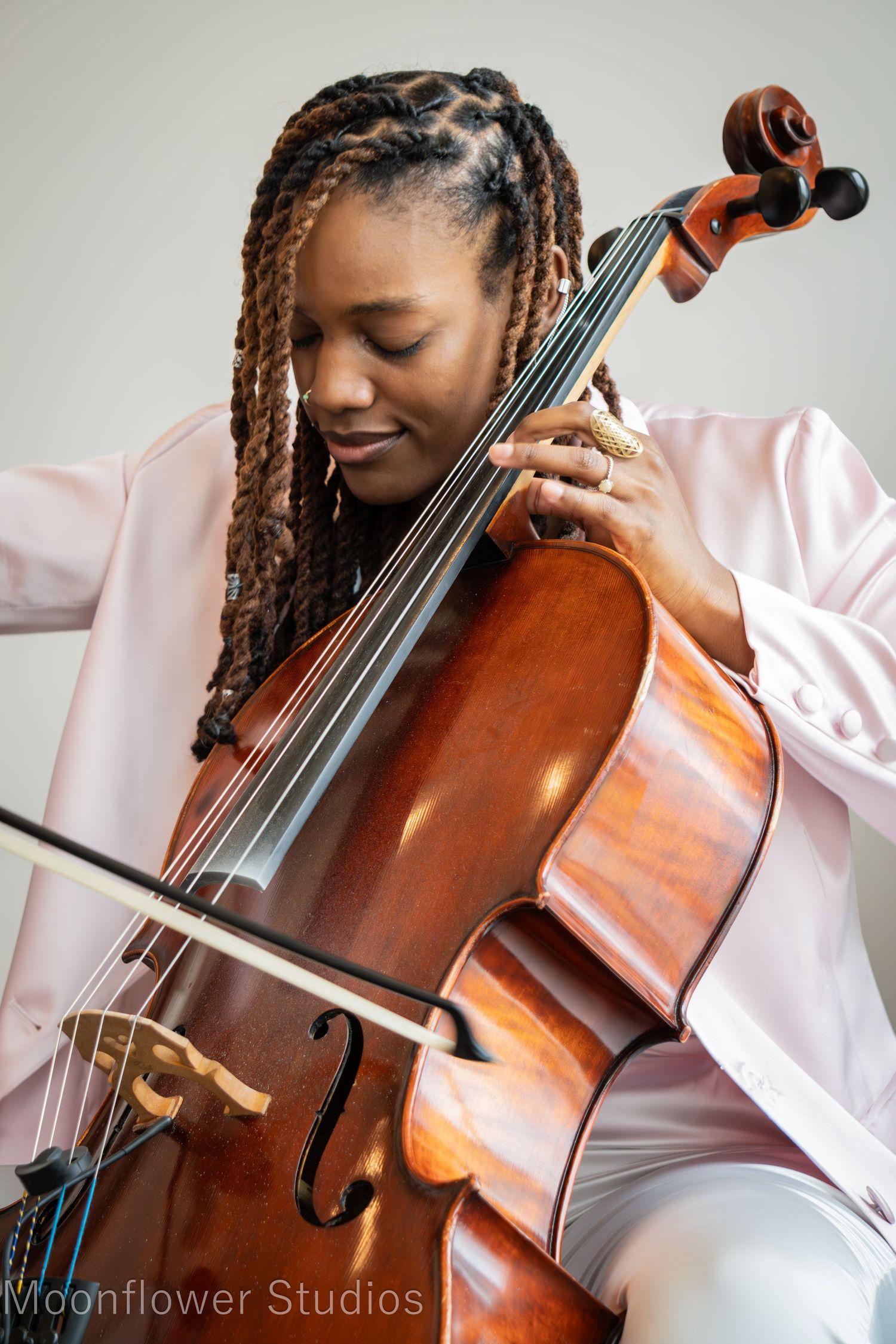 A musician plays a wooden cello while wearing a white button-down shirt.