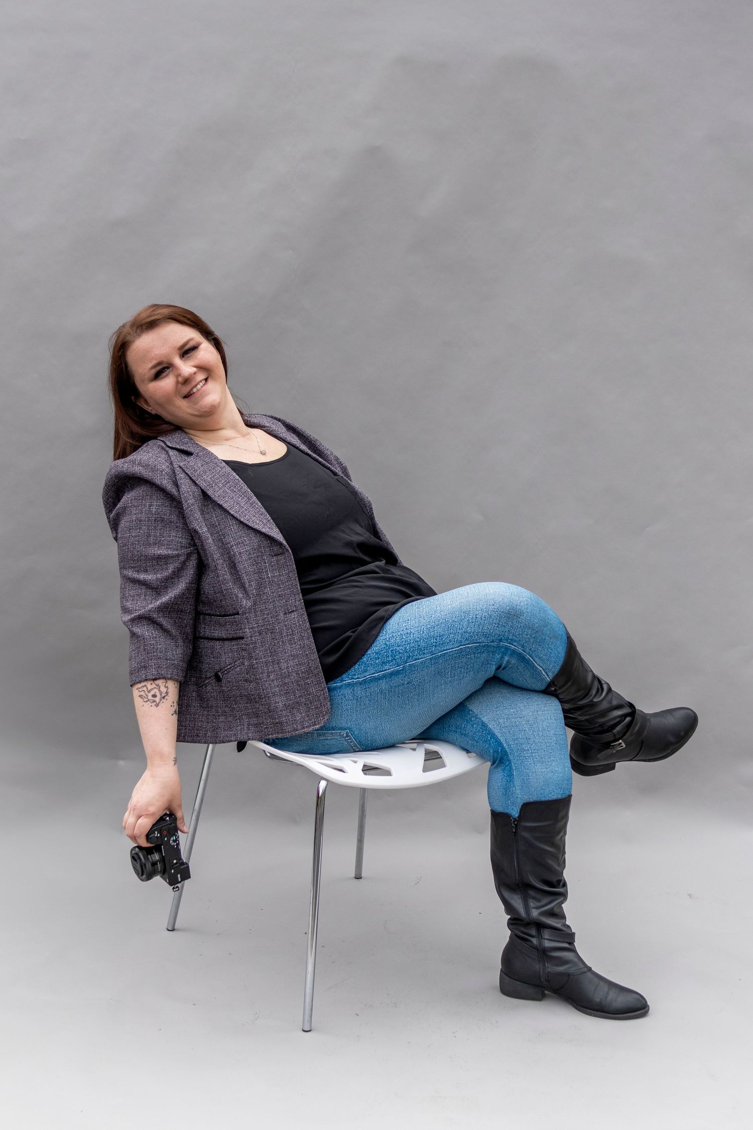 Professional studio portrait poses showing casual comfort on a modern chair against gray backdrop.