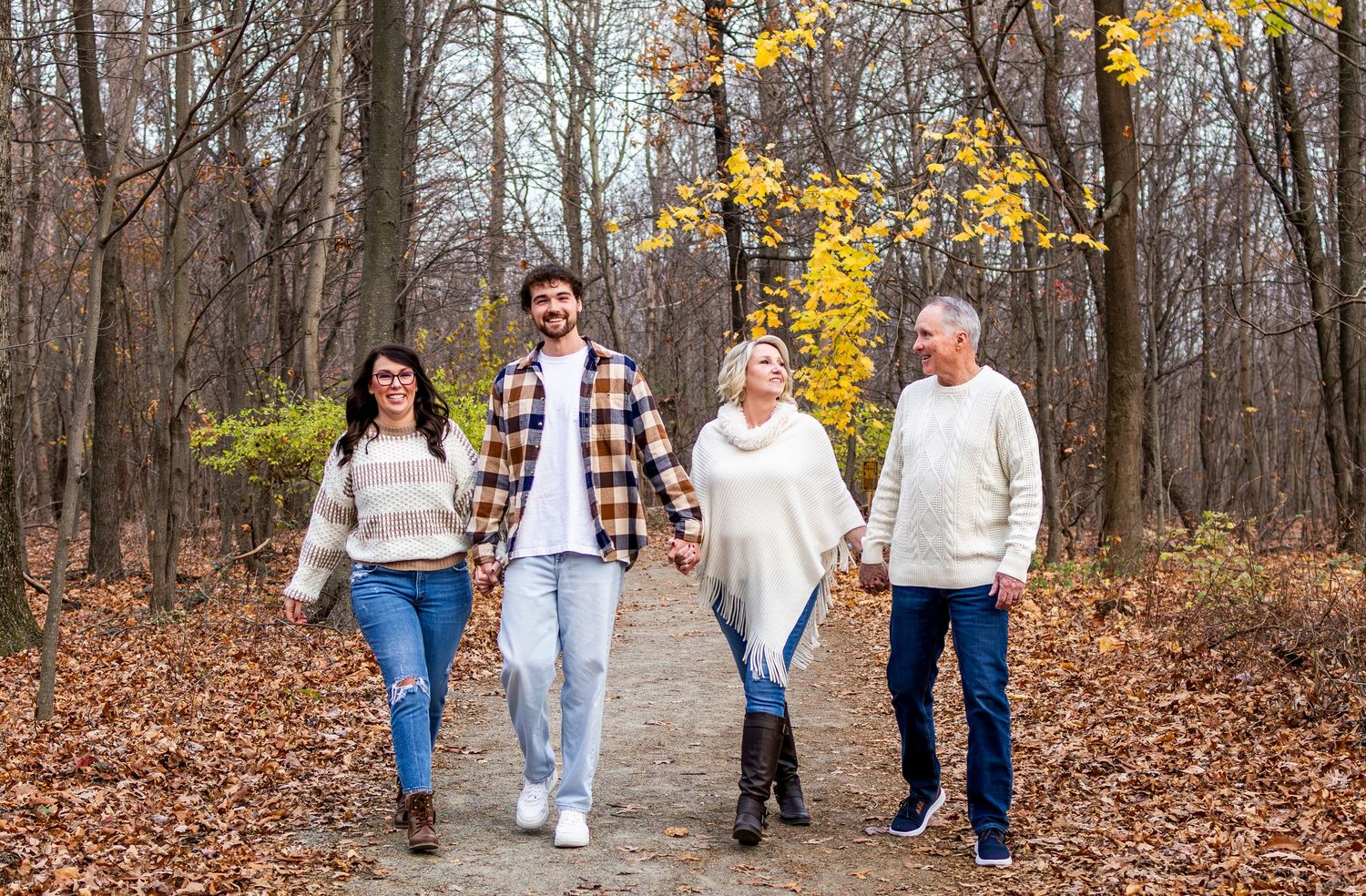 Family walking together through a wooded autumn trail with fallen leaves on the ground.