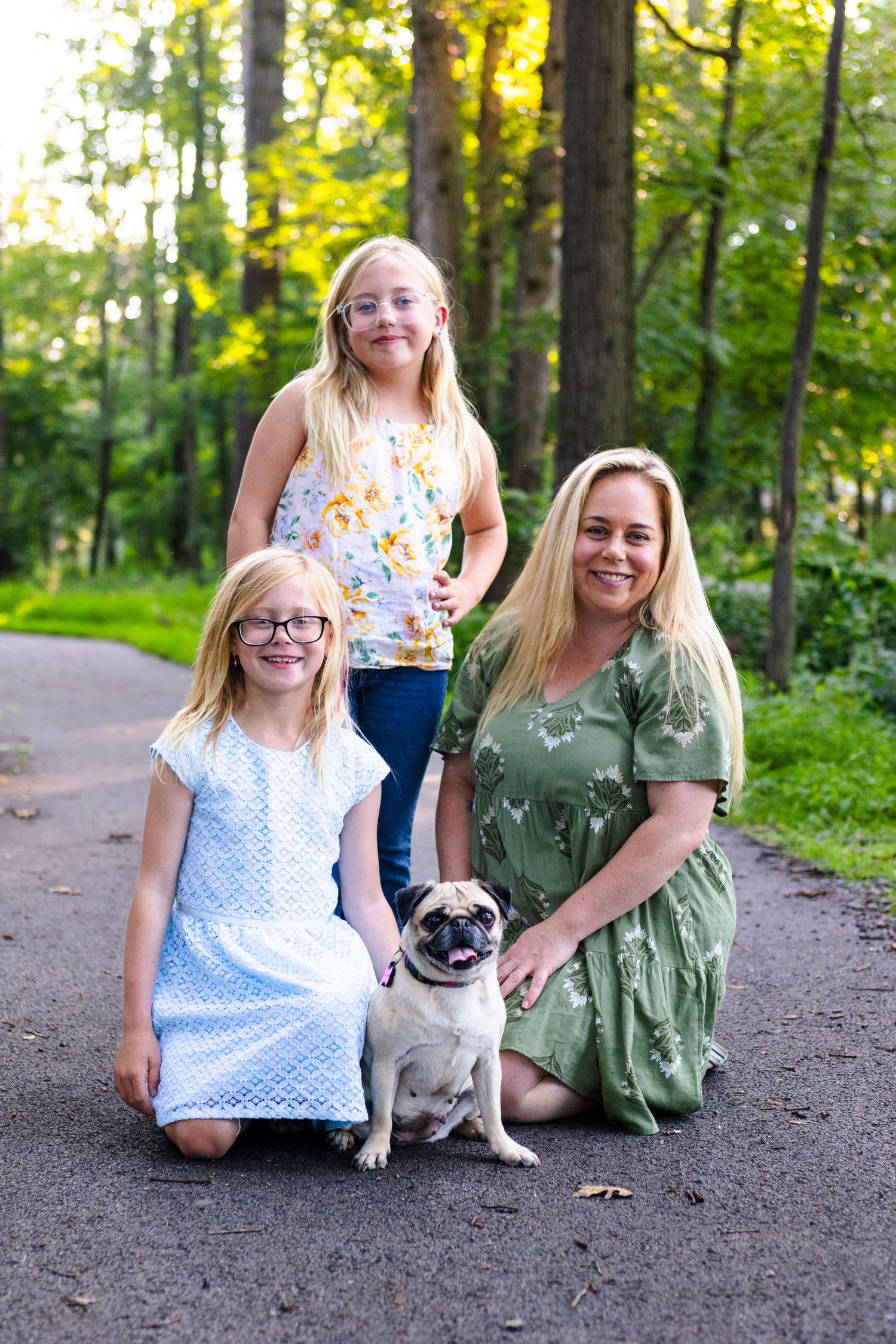 Family and their dog pose together on a forest path during golden hour.