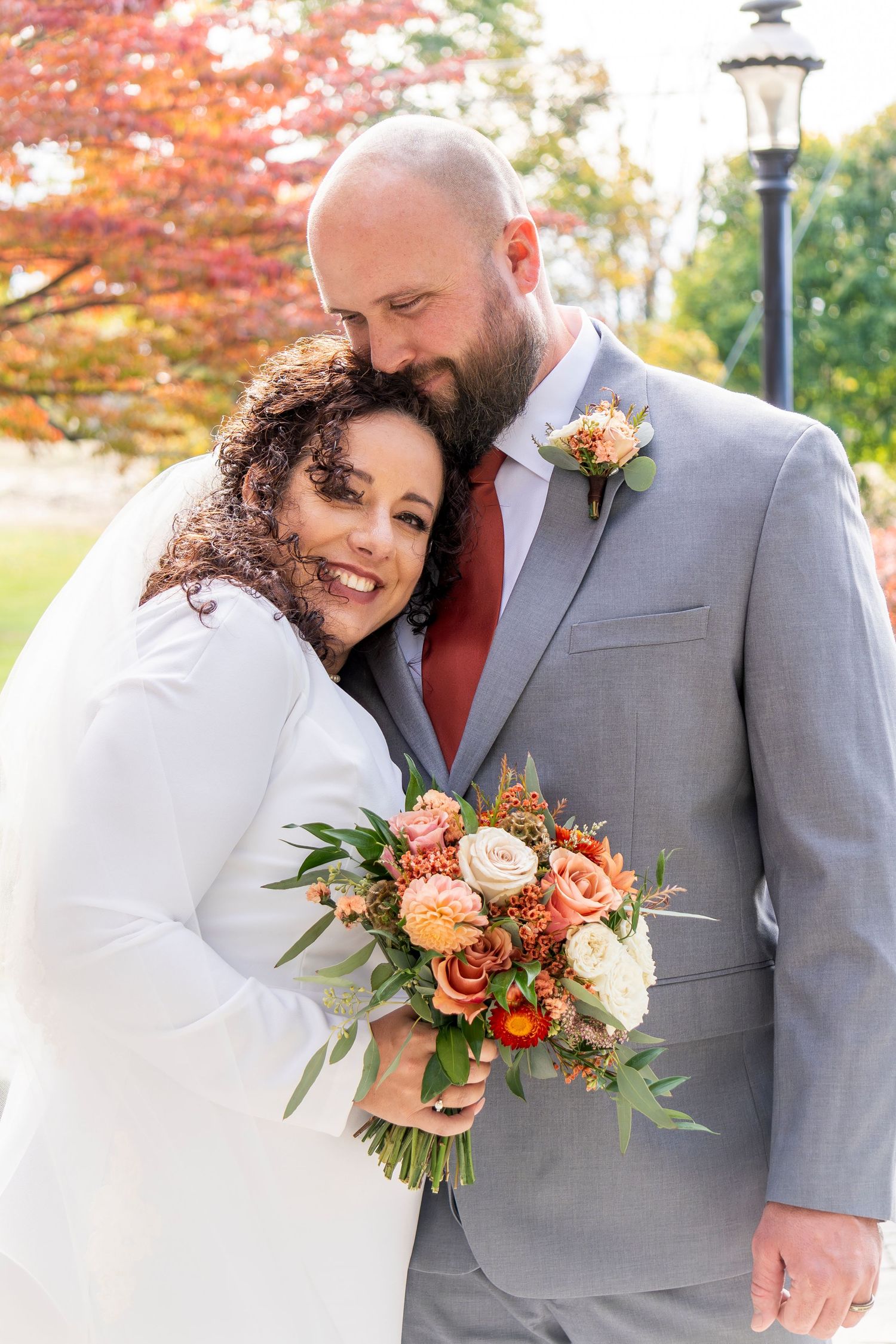 Romantic autumn wedding photos with beautiful orange and white floral bouquet against fall foliage.