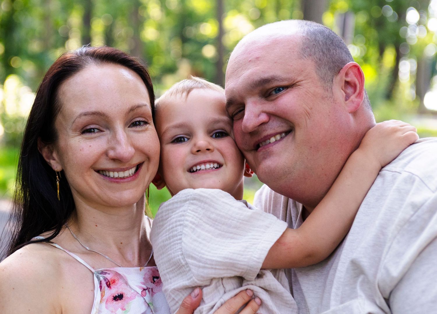 A joyful family shares laughter and embraces while walking together on a wooded path in bright sunlight.