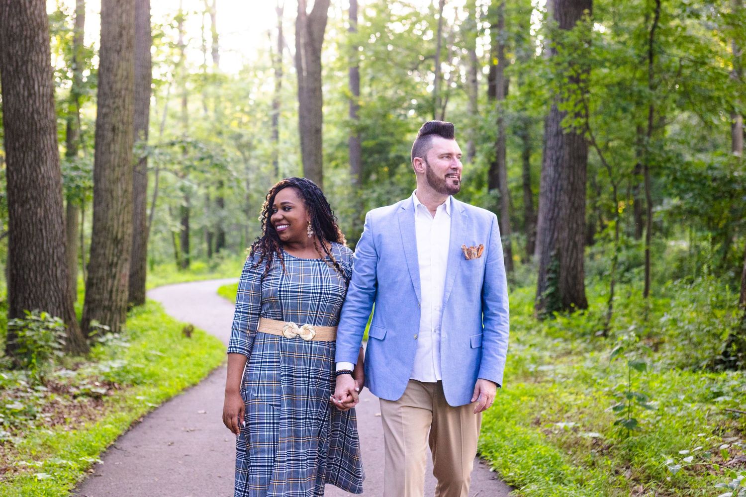 Couple walking together on a tree-lined path during an outdoor photo session.