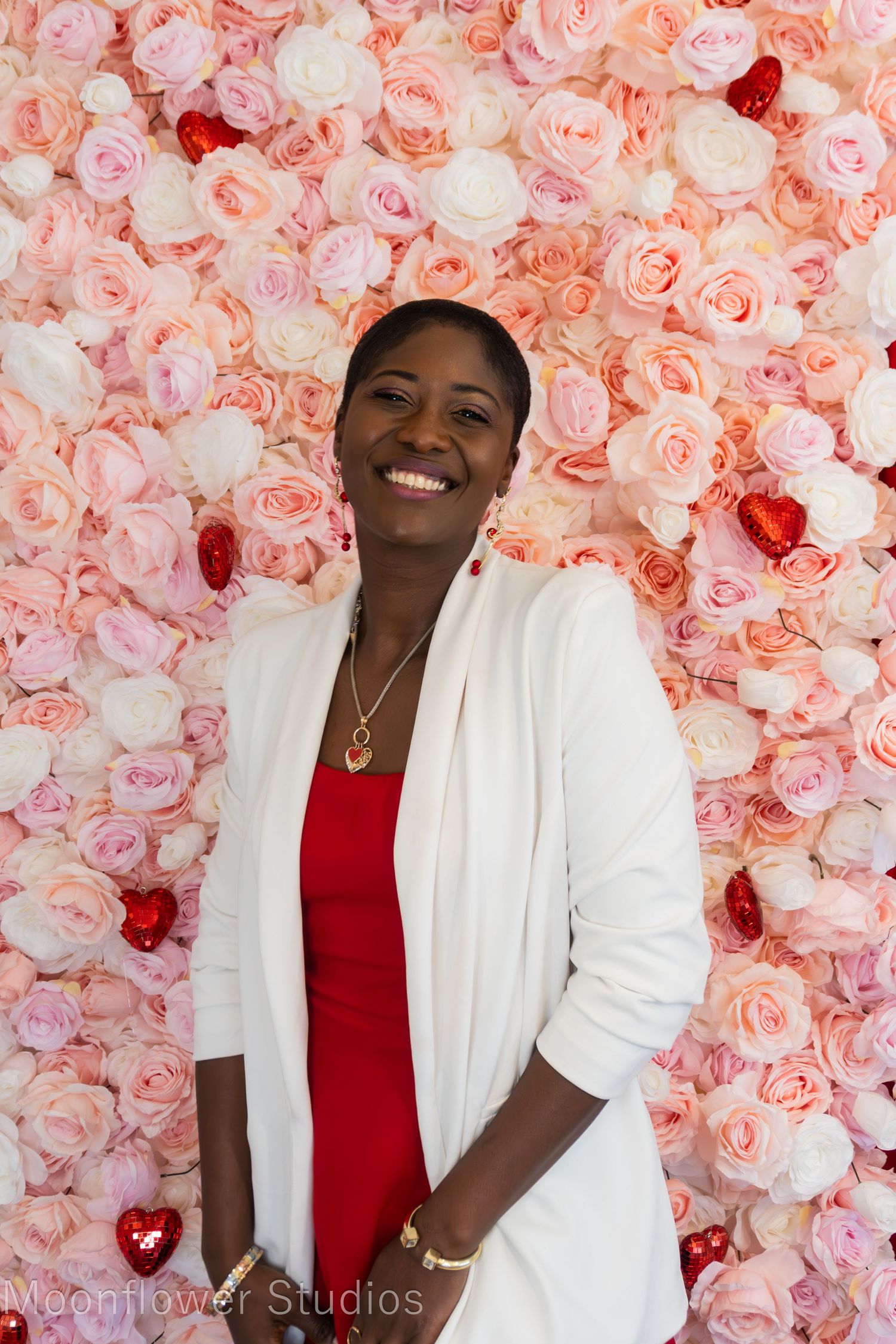 Professional portrait against a pink floral wall backdrop featuring elegant white and red attire.