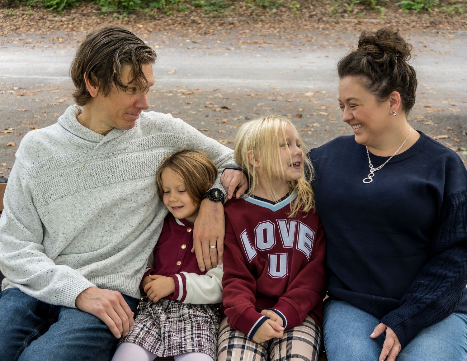 Family members sit together on a bench wearing casual clothing in burgundy and grey tones.