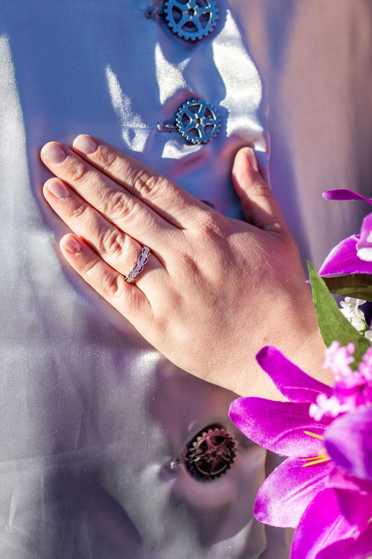Close-up of hands with rings against purple flowers in soft lighting.