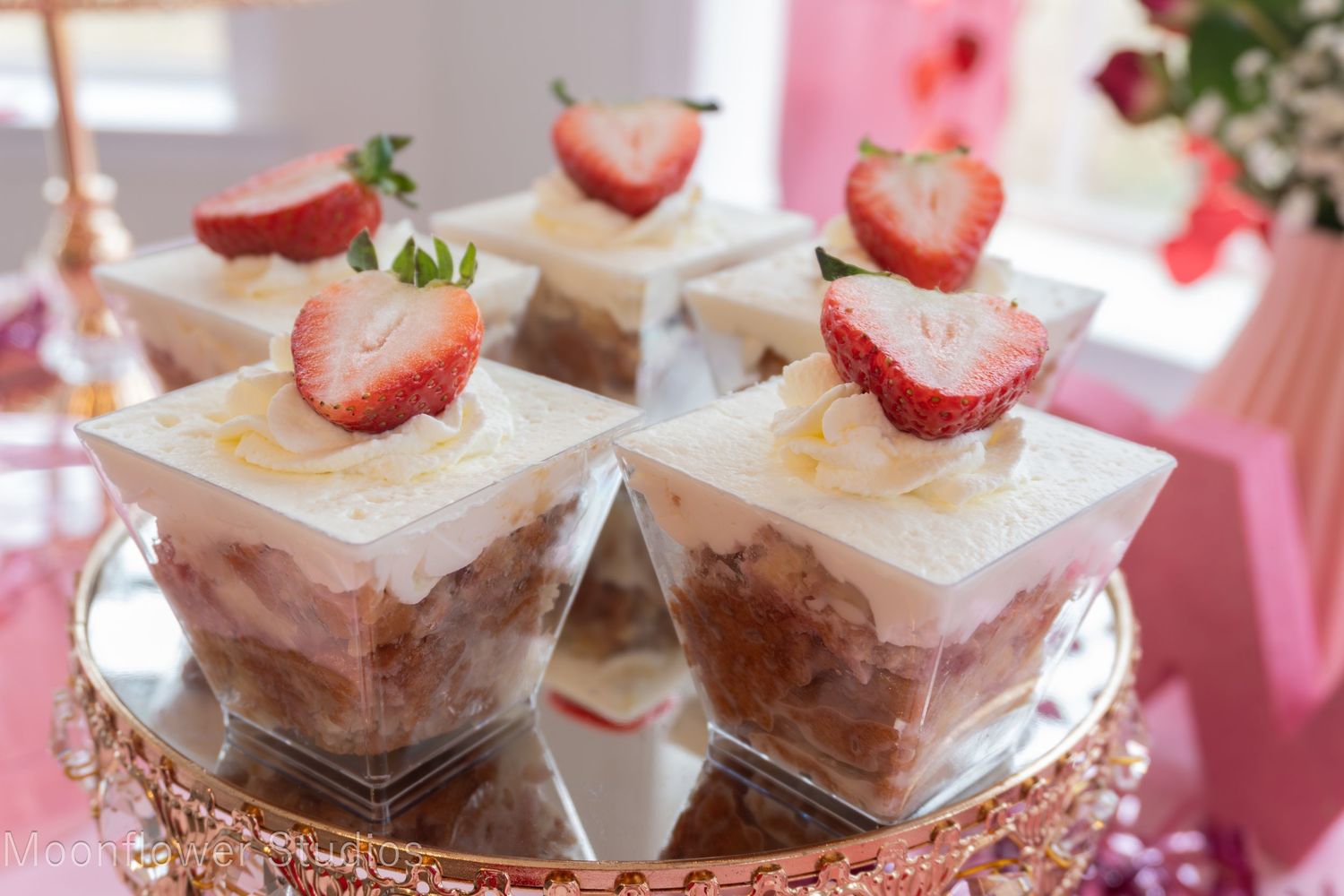 Elegant dessert display featuring strawberry-topped mini parfaits on a decorative tray.
