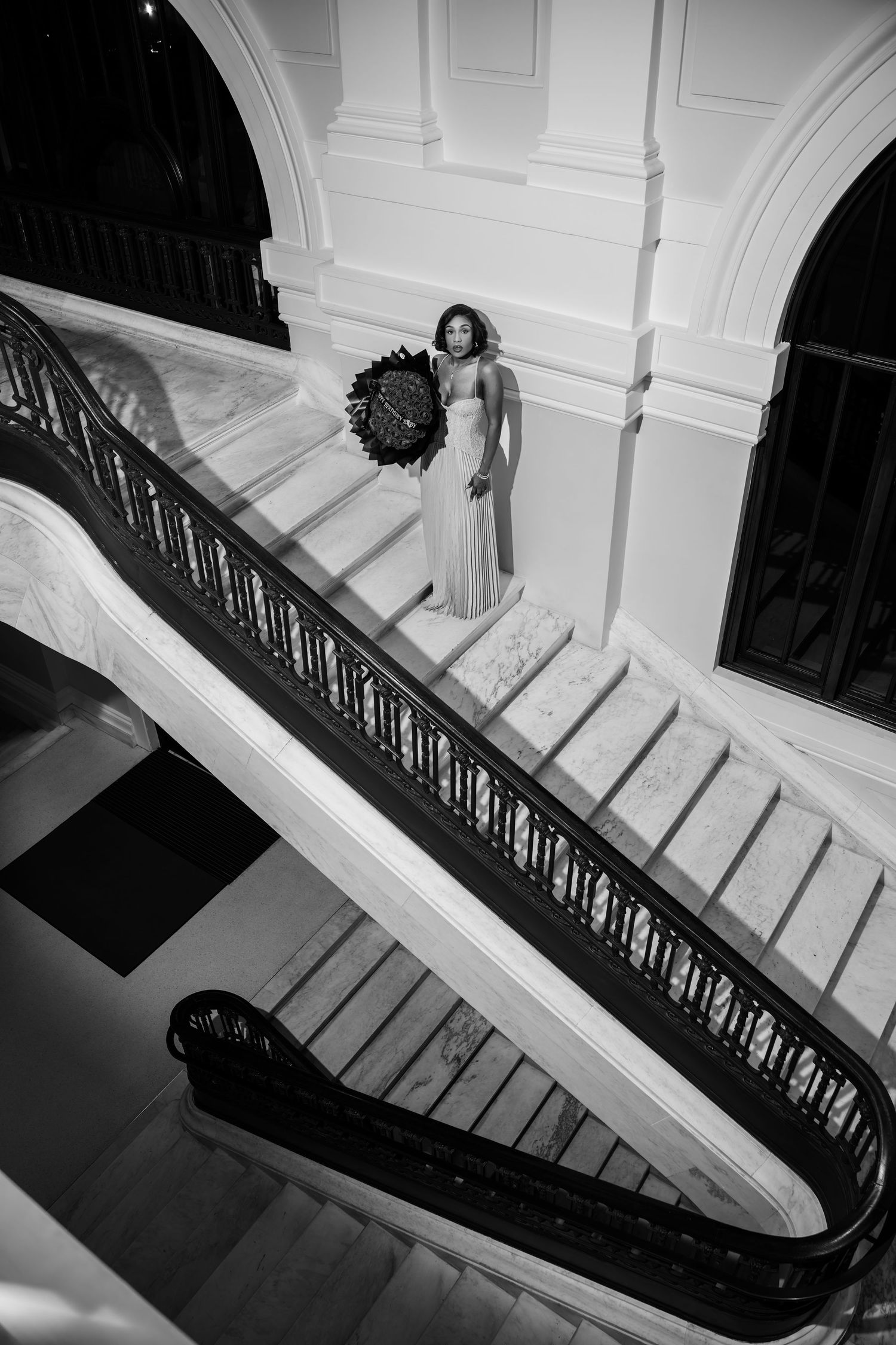 Black and white architectural photo showing elegant curved staircase with ornate railing casting dramatic shadows.