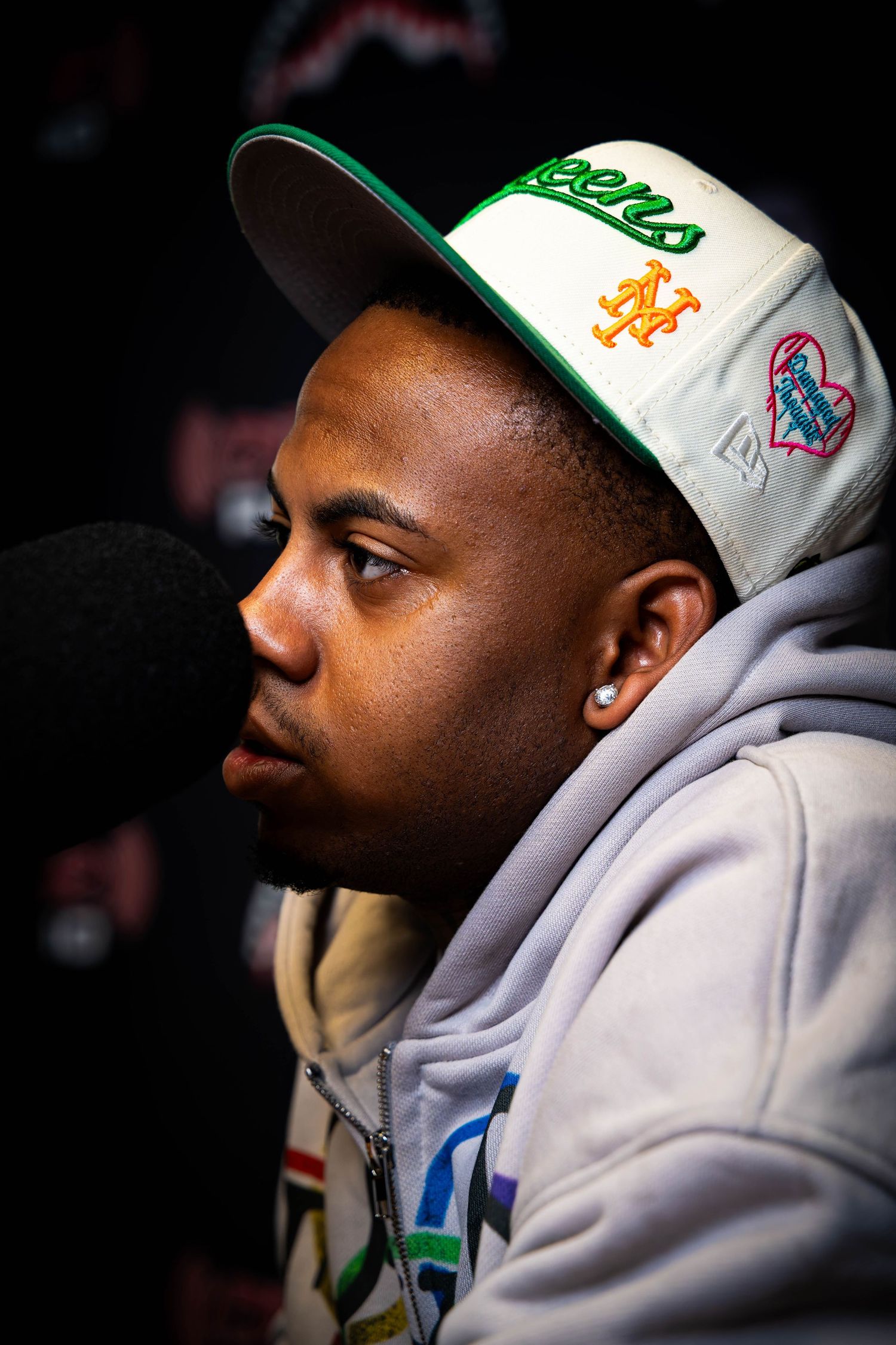 Person in white baseball cap with NY Mets logo wearing grey hoodie in profile view.