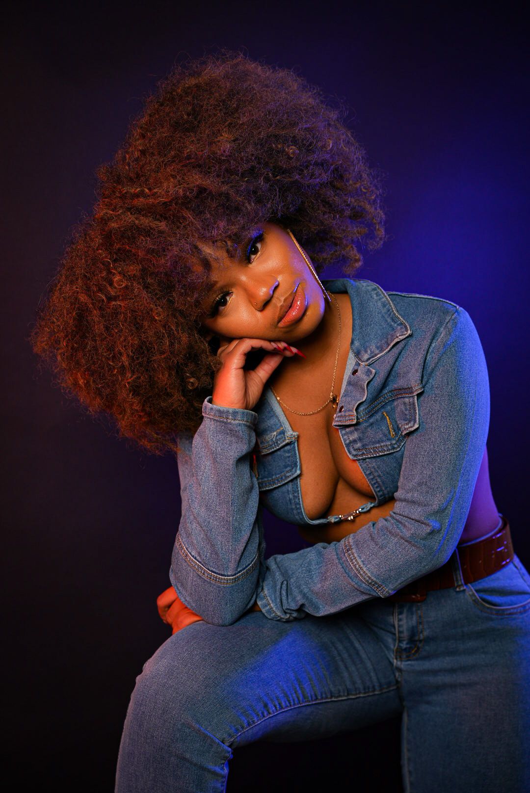 Artistic portrait with blue lighting and denim jacket against dark background.