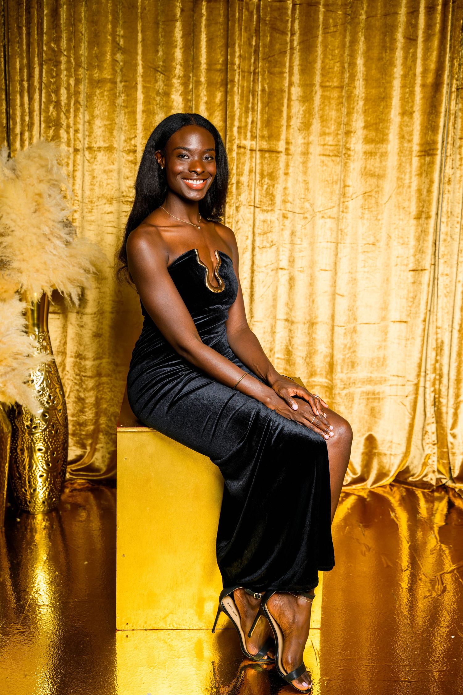 Client in black dress poses elegantly against shimmering gold backdrop.