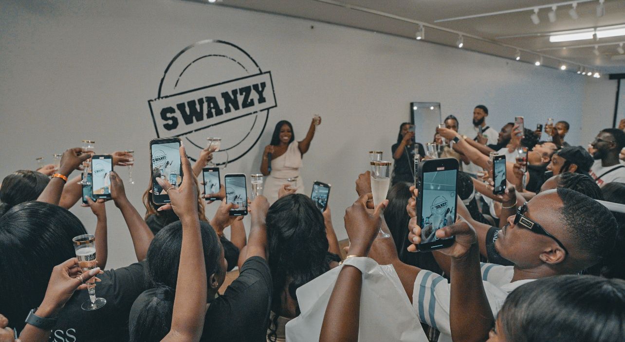 Crowd of excited fans holding up phones at event with Swanzy logo visible.