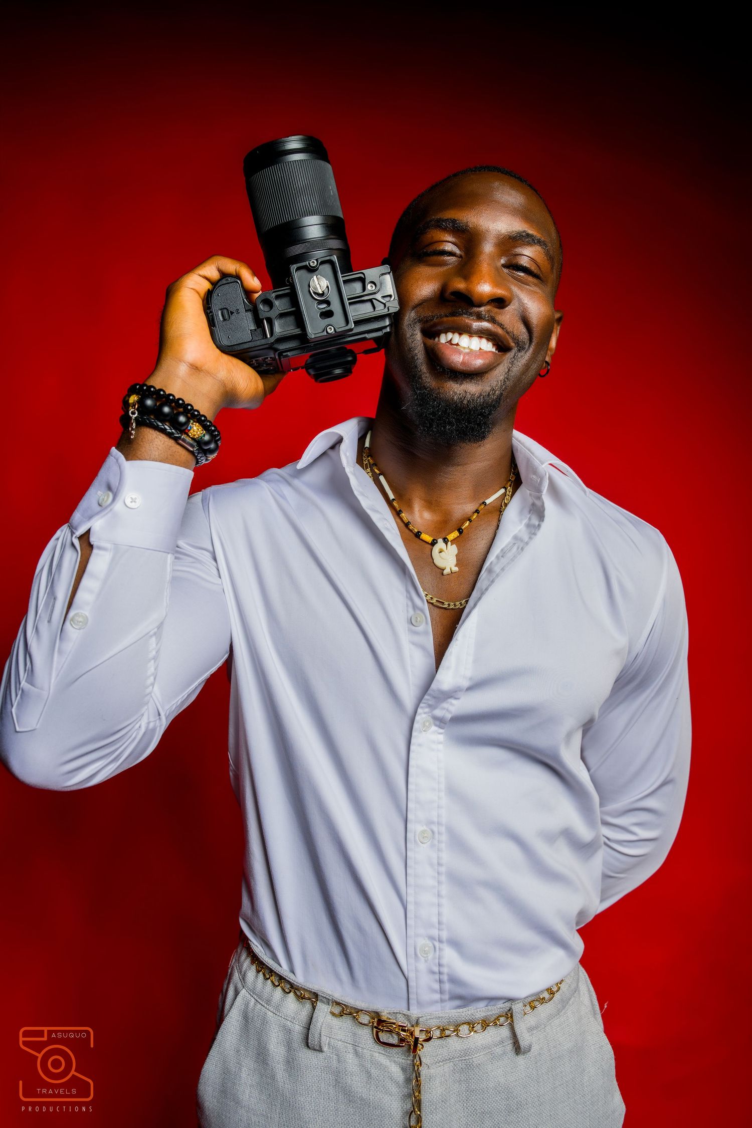 Photographer in white shirt holding camera equipment against red backdrop.