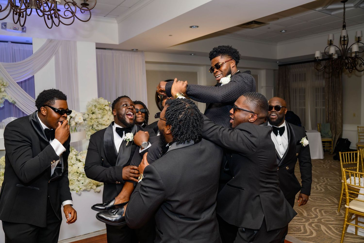 Wedding party members in black formal attire dancing and celebrating.