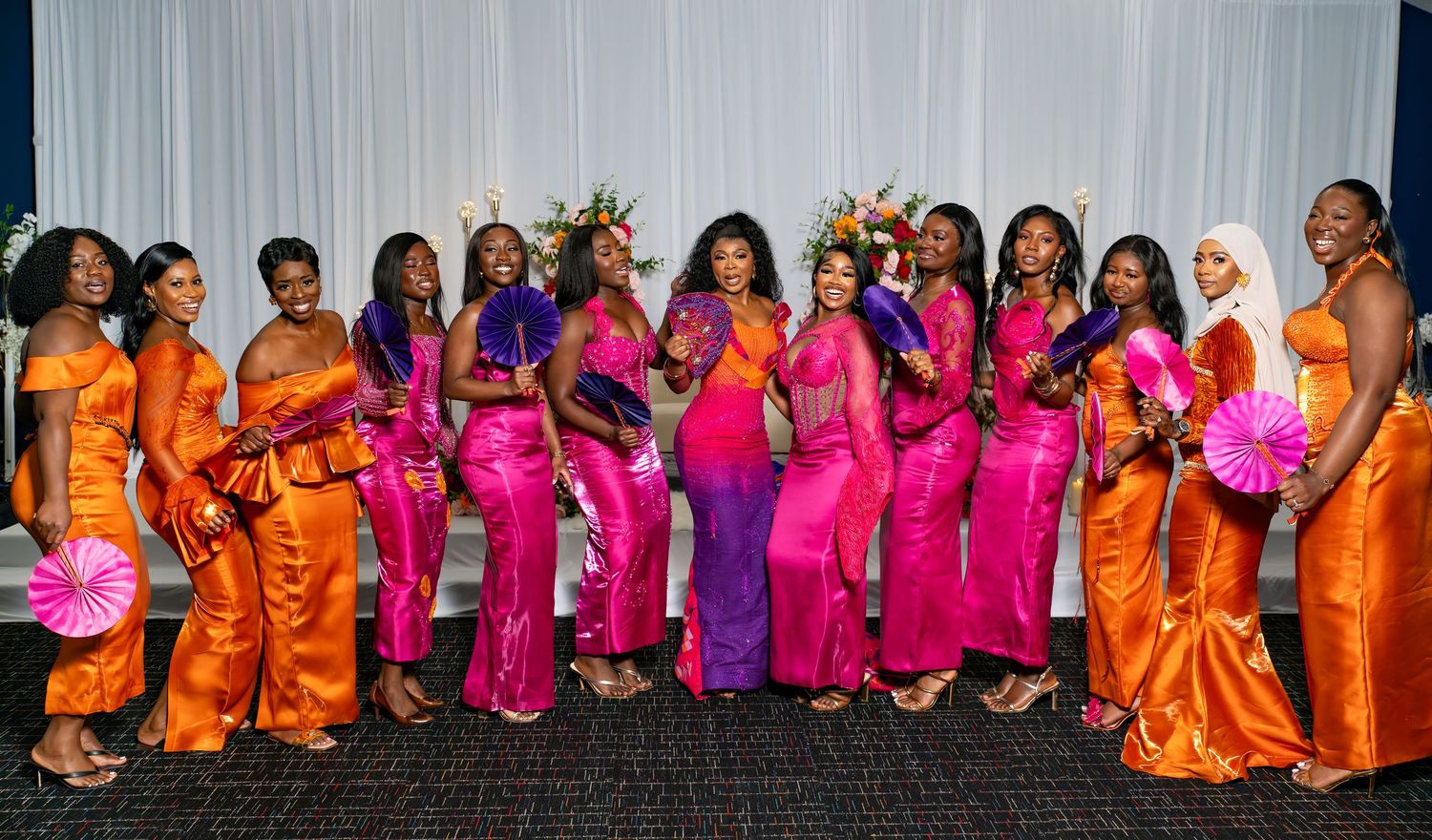 Wedding party members in orange and pink dresses pose together for a celebratory photo.