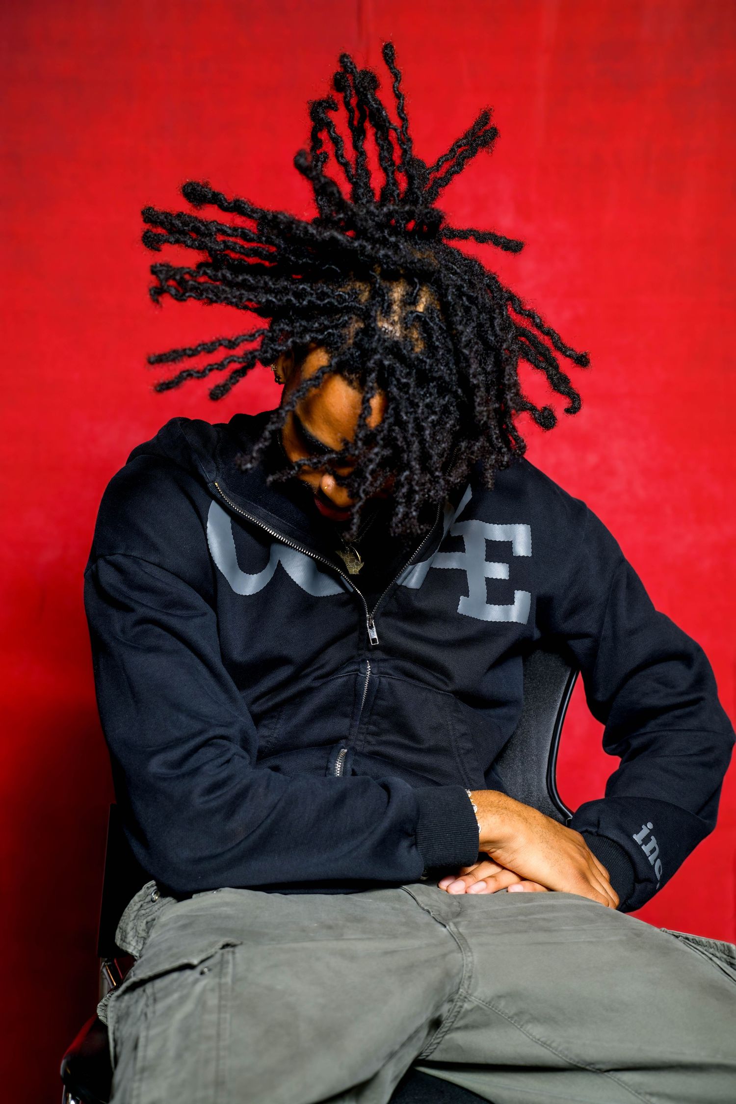 Person in black jacket with dreadlocks against vibrant red background in artistic portrait series.