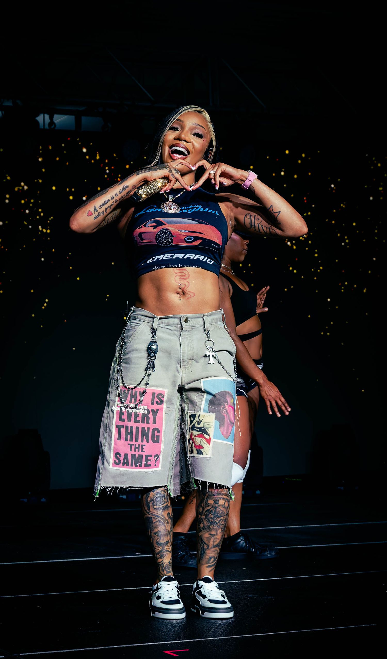 Performer in distressed denim and graphic tee dancing on dark stage.