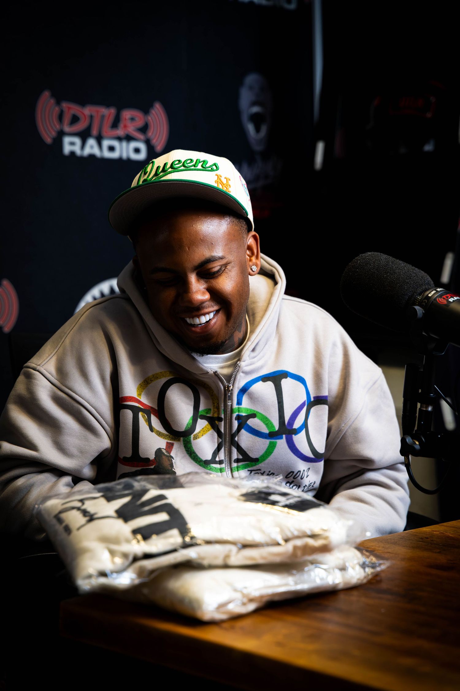 Guest laughing during radio interview wearing white hoodie with colorful logo.