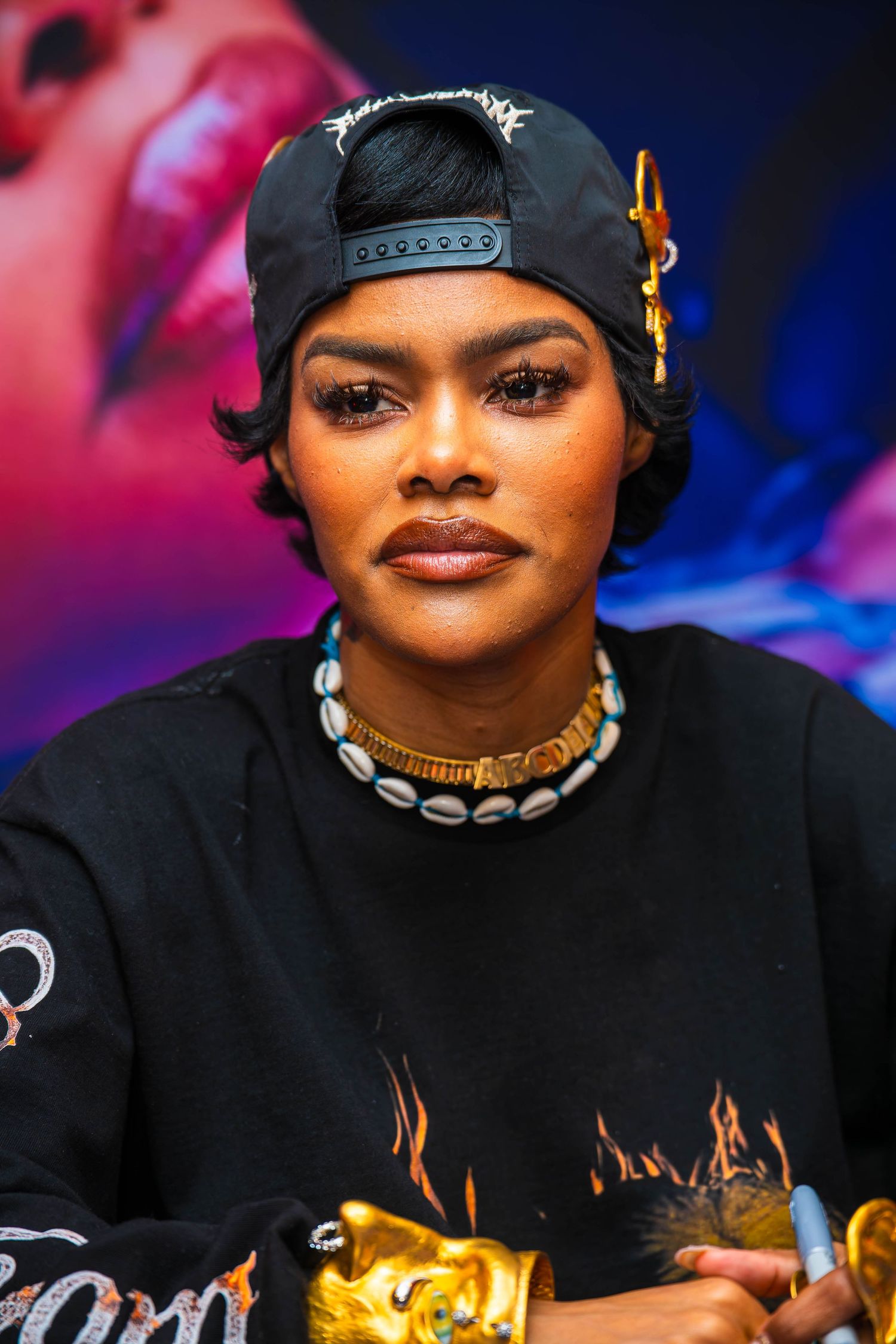 Artist signing merchandise while wearing a black cap and necklace at an event with colorful lighting.