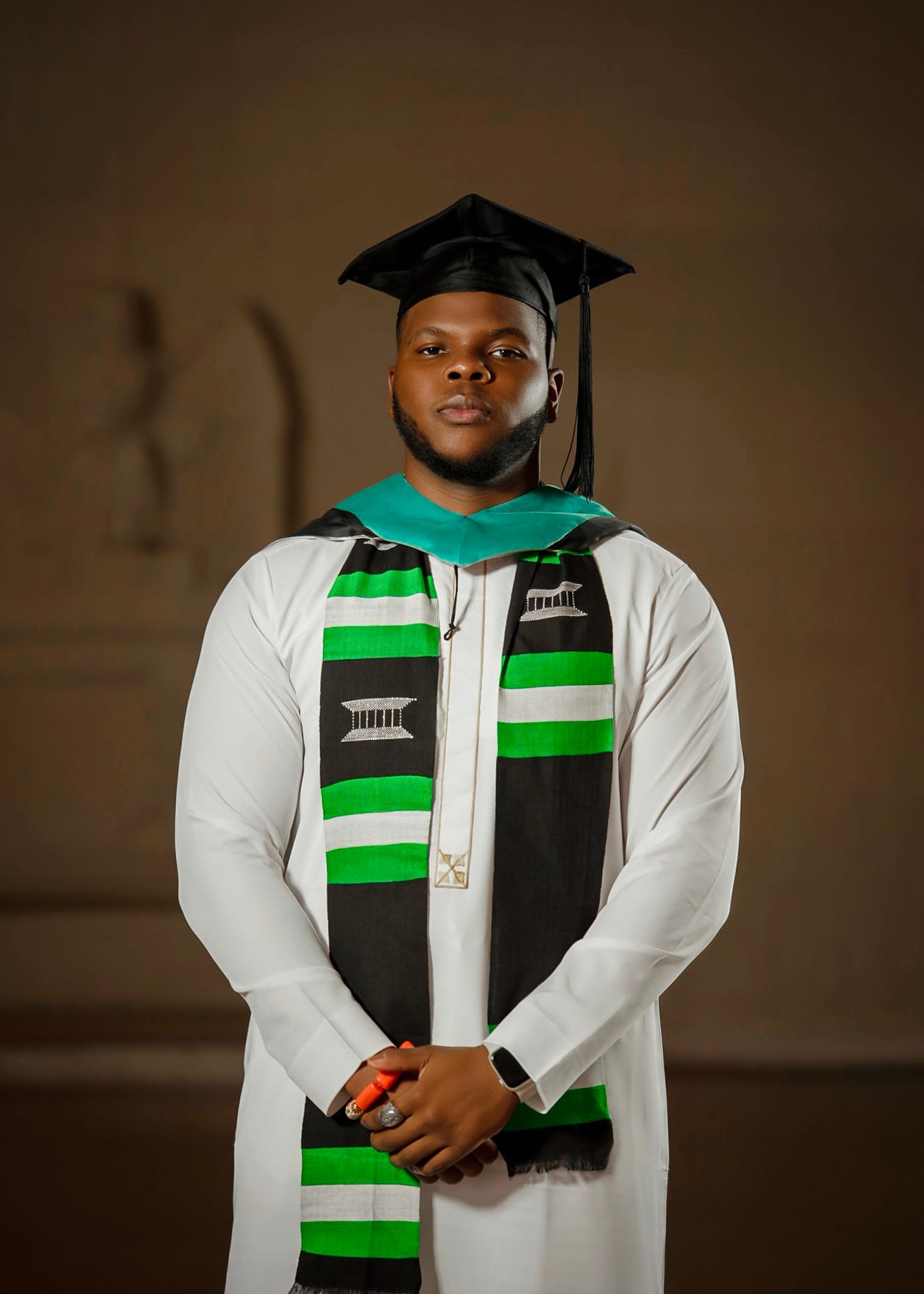 Graduate in white academic regalia with green and black stole and graduation cap.