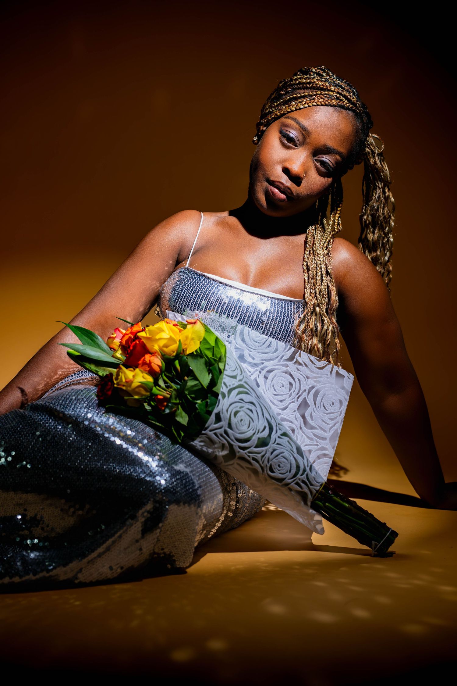 Artistic portrait of person in silver dress with flowers lying on brown background.