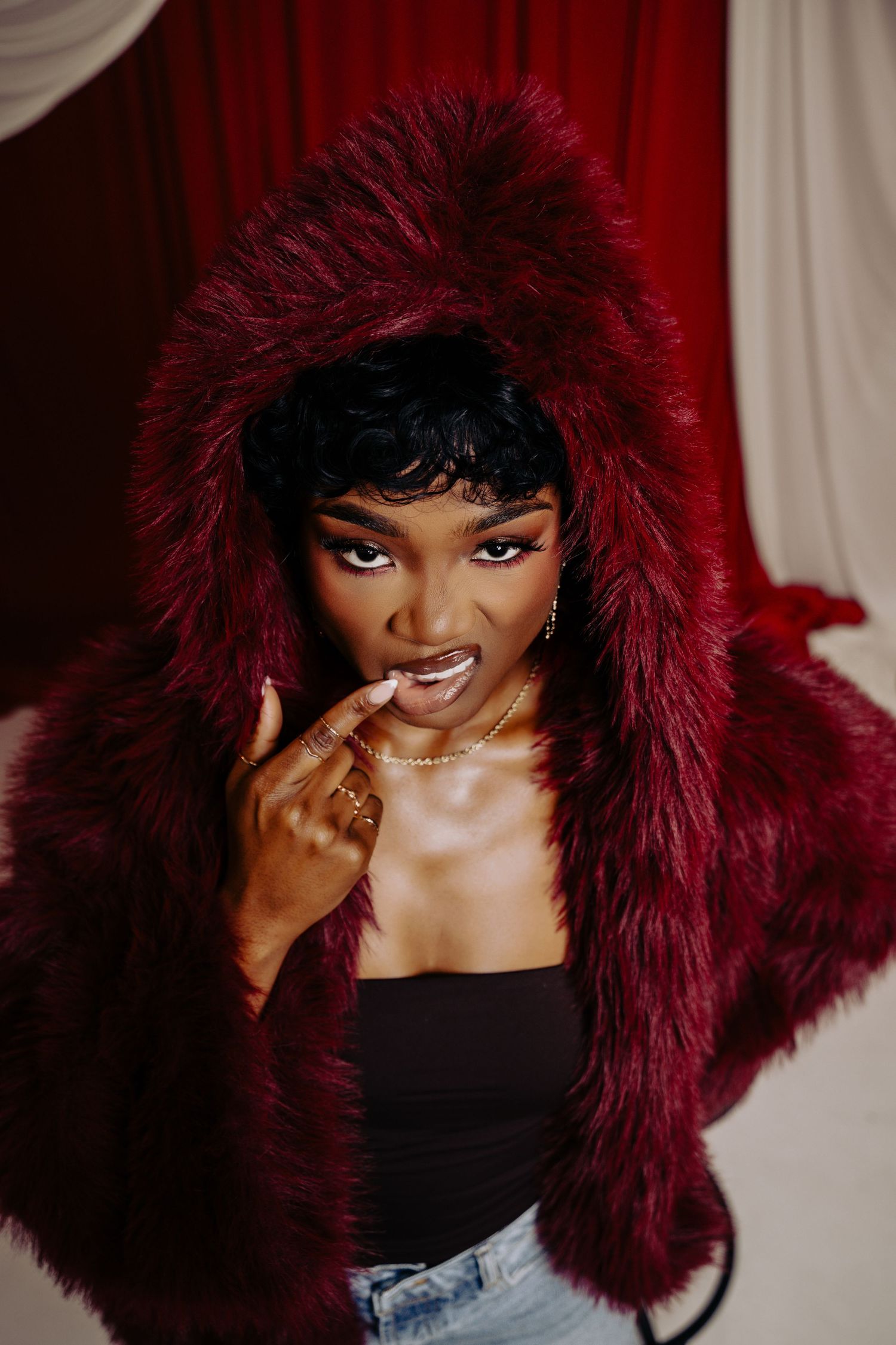 A fashion photo series showing a model wearing a burgundy fur-trimmed hood and black top in different poses.