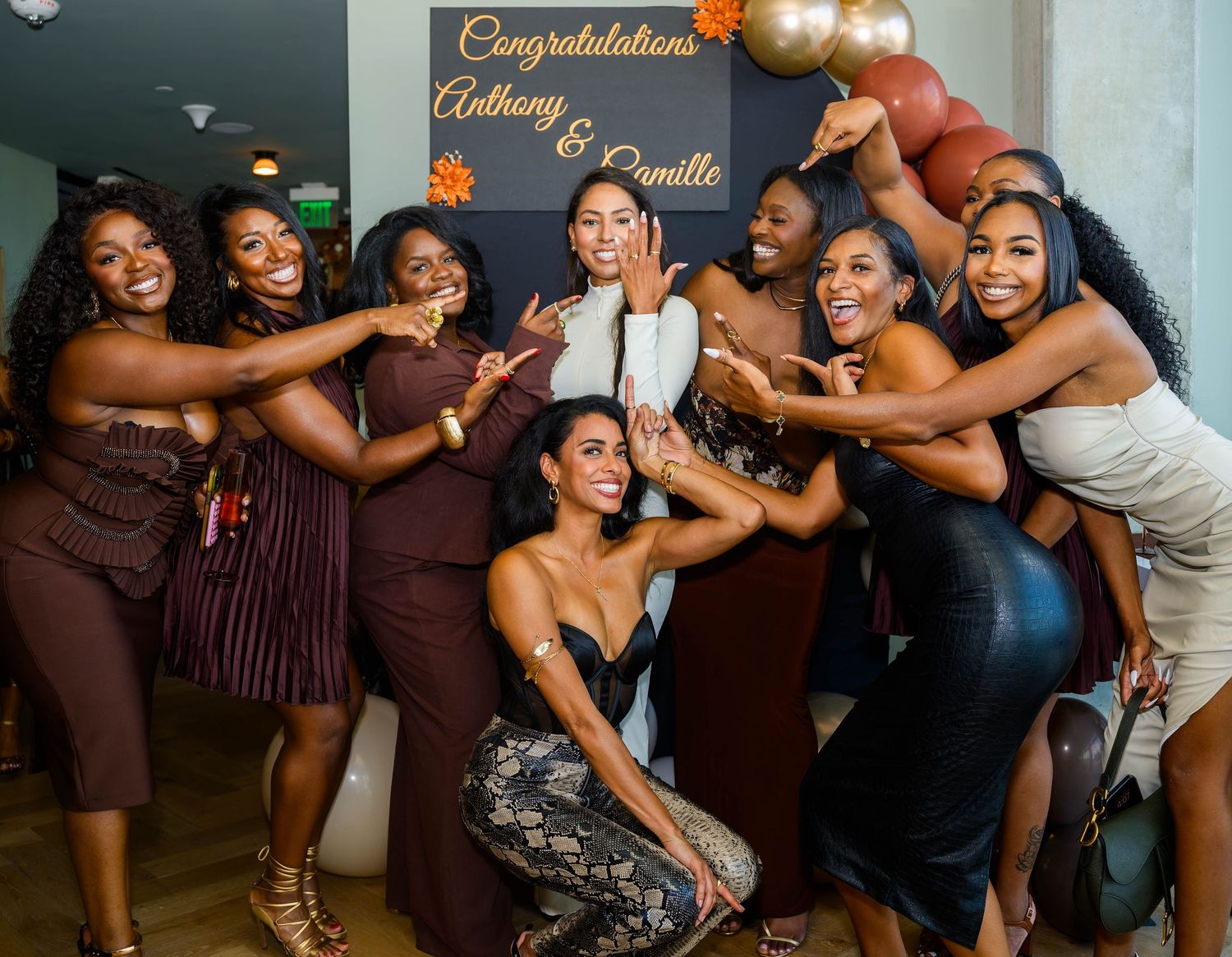 A joyful celebration party scene with friends posing playfully in front of a congratulations sign and balloons.