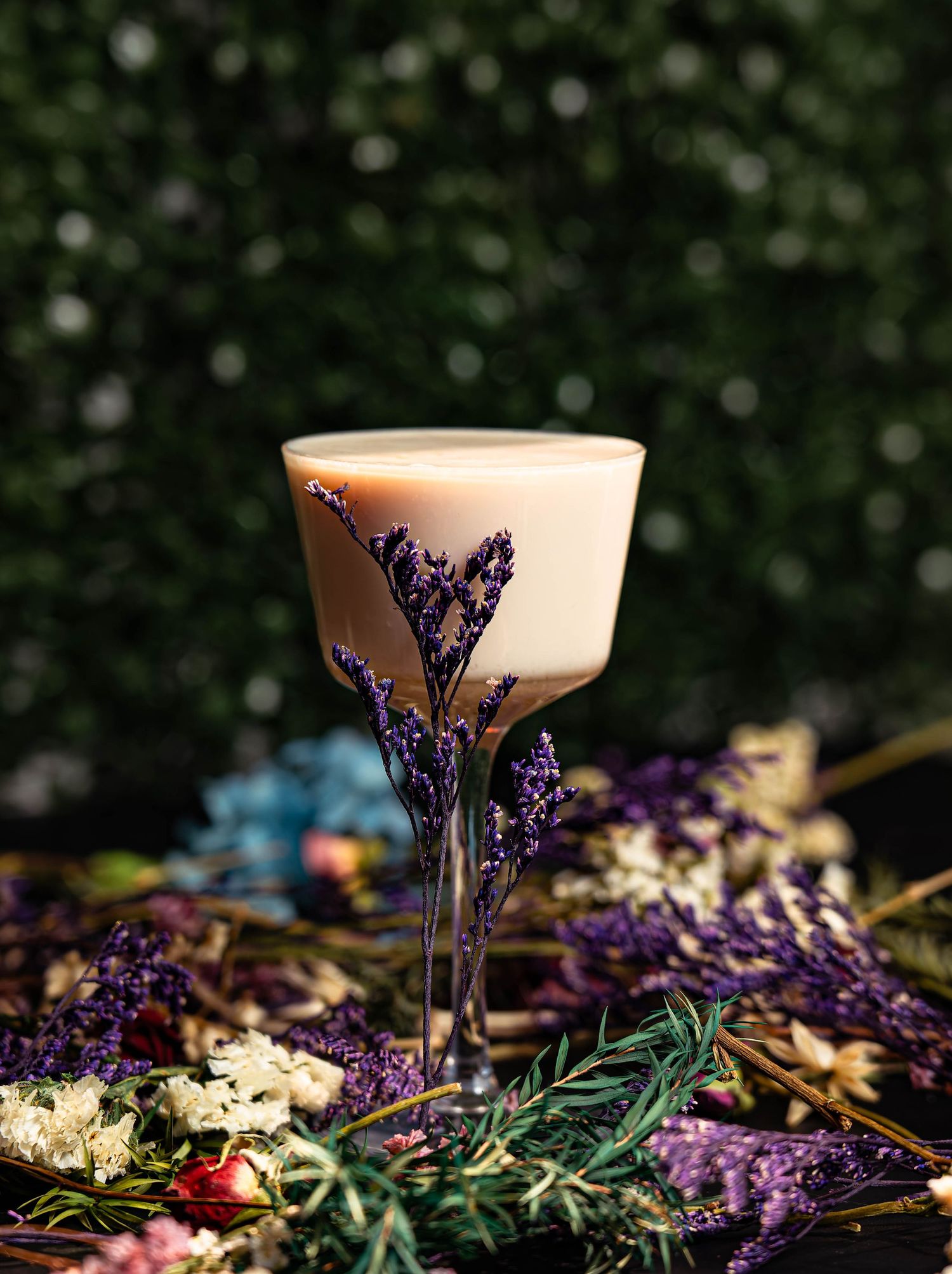 Elegant cocktail glass with purple lavender sprigs and floral decorations against dark bokeh background.