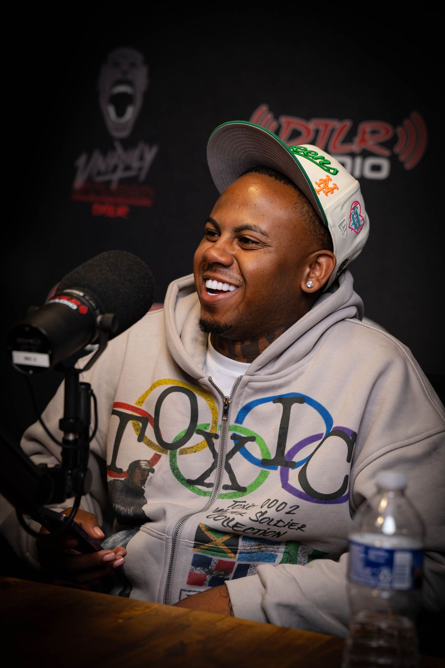Radio guest smiling during interview wearing grey hoodie and baseball cap.