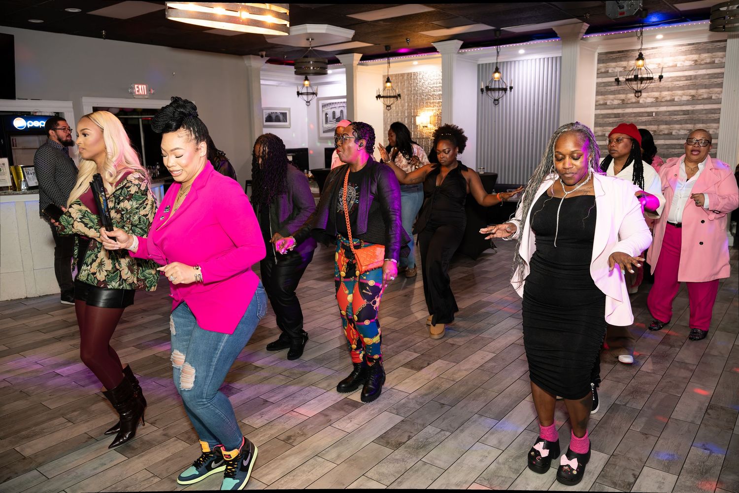 People dancing and moving on a wooden floor with purple lighting effects.
