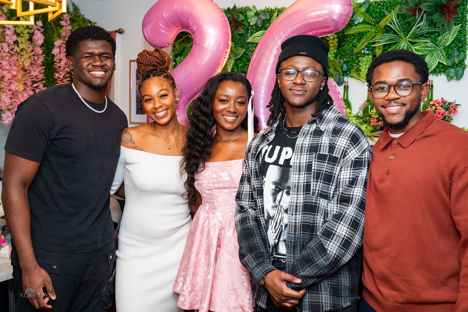 Friends gather for a celebration with pink number balloons and floral decorations.