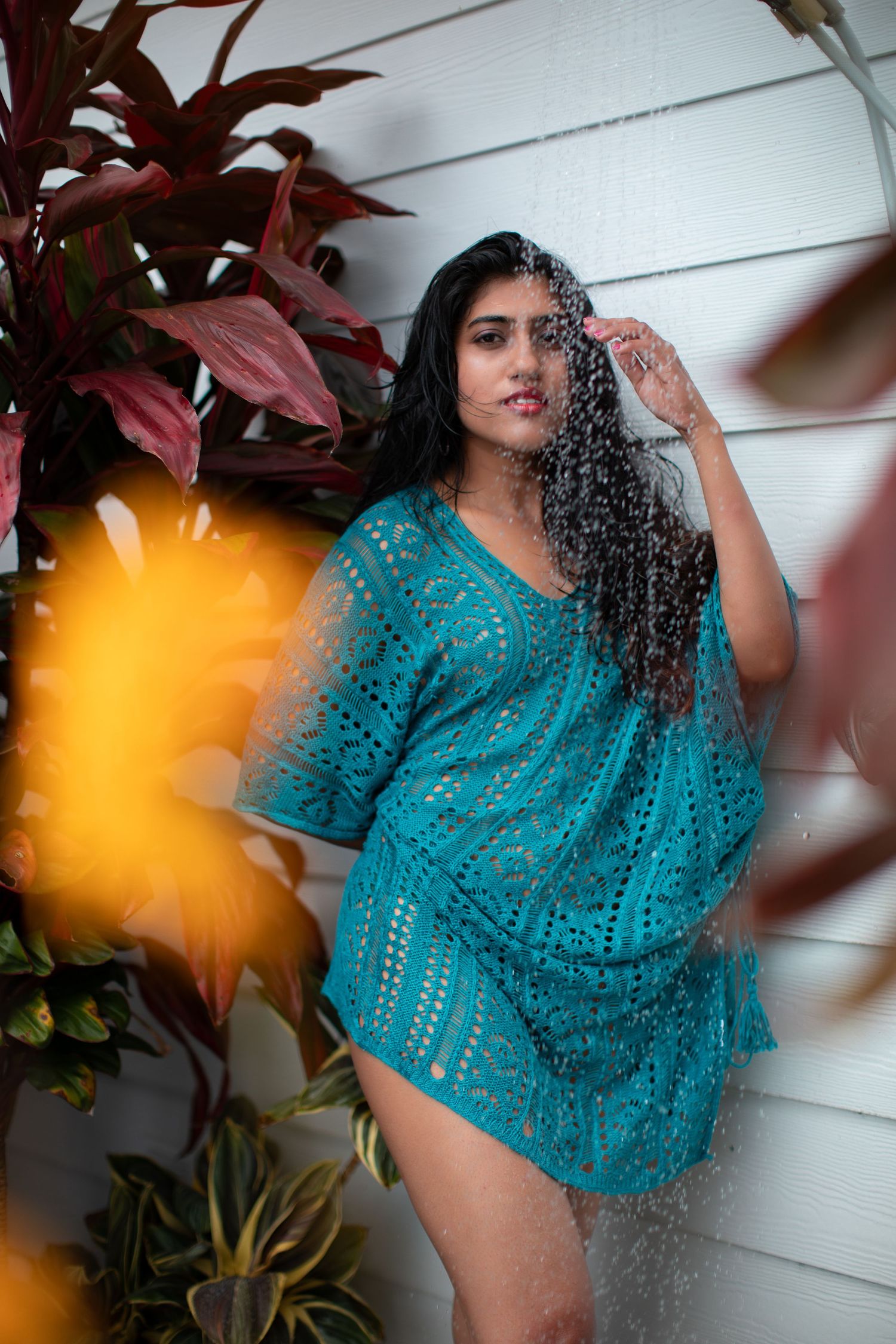 Fashion portrait featuring a turquoise lace cover-up against a white wall with red plants.