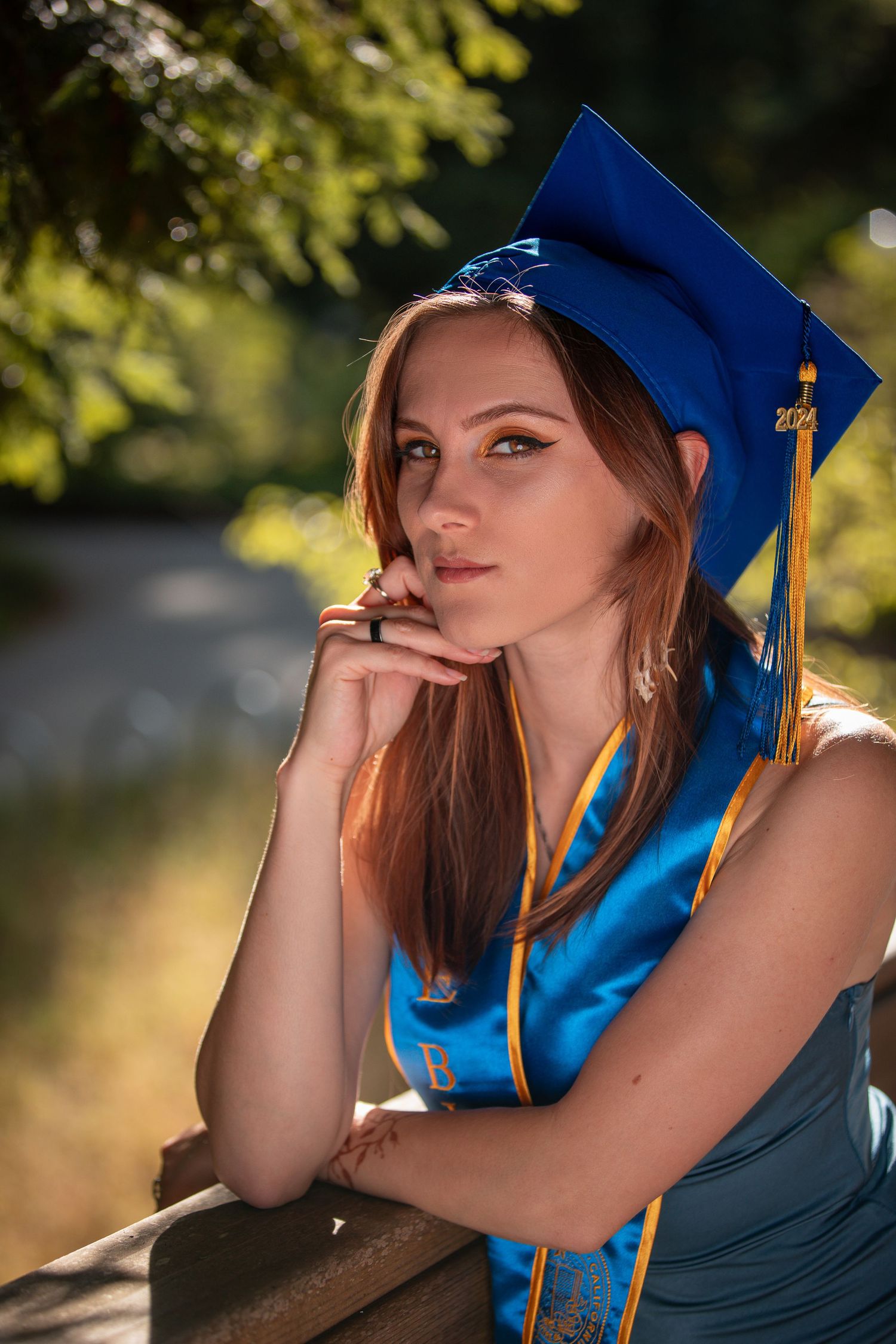 Close-up portrait of graduate wearing blue cap with gold tassel against blurred natural background.