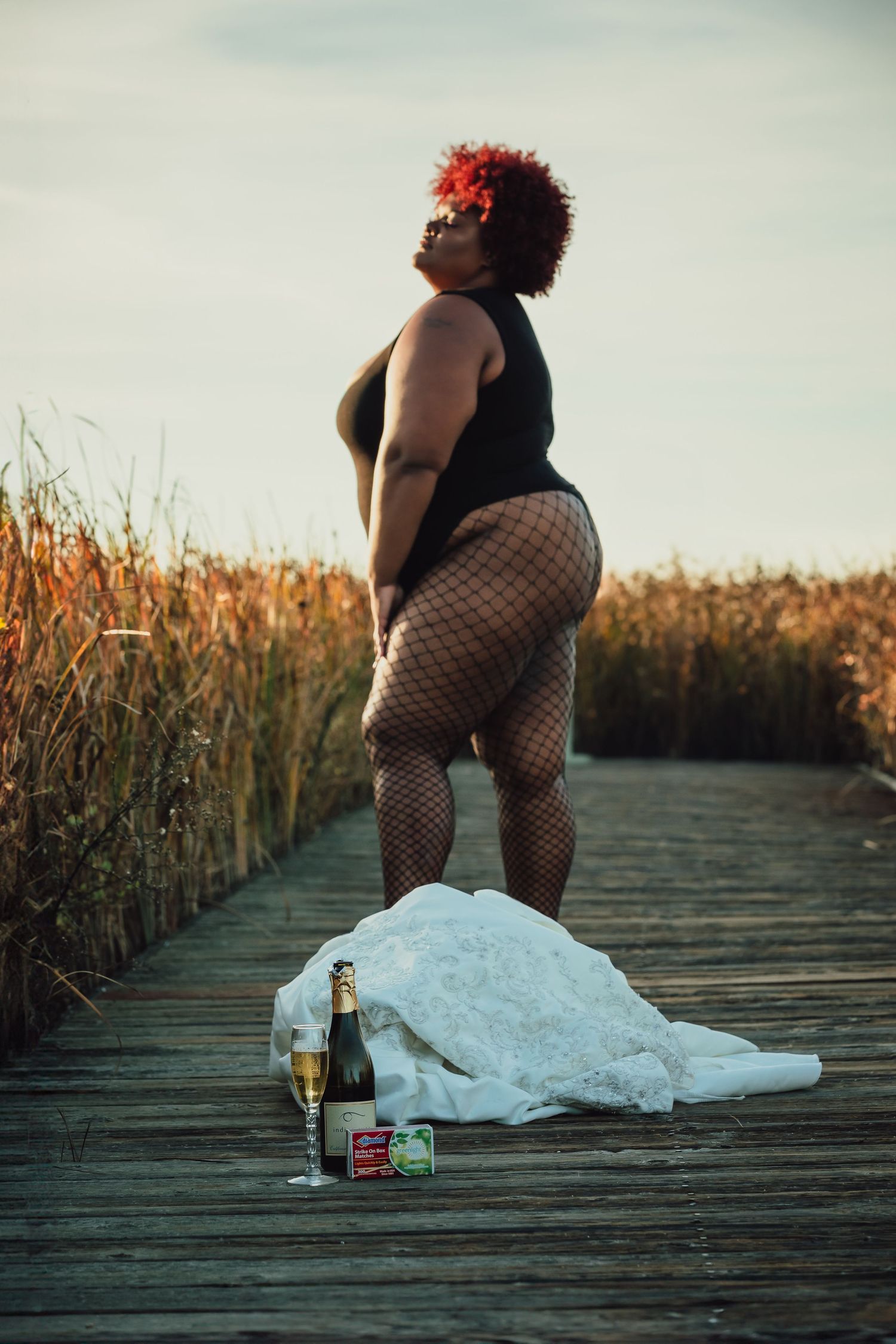 A white dress lies on a wooden boardwalk with bottles at sunset.