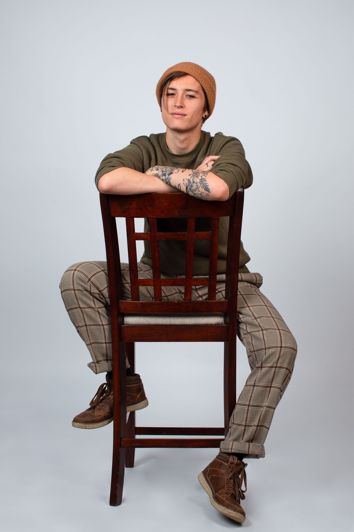 Creative poses on wooden chair wearing plaid pants and brown beanie in studio setting.