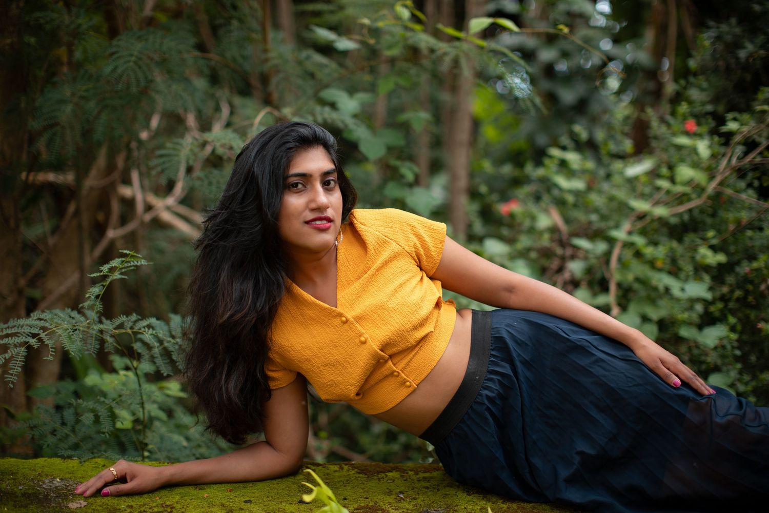 Person in yellow top and dark pants poses gracefully against a lush green forest background.
