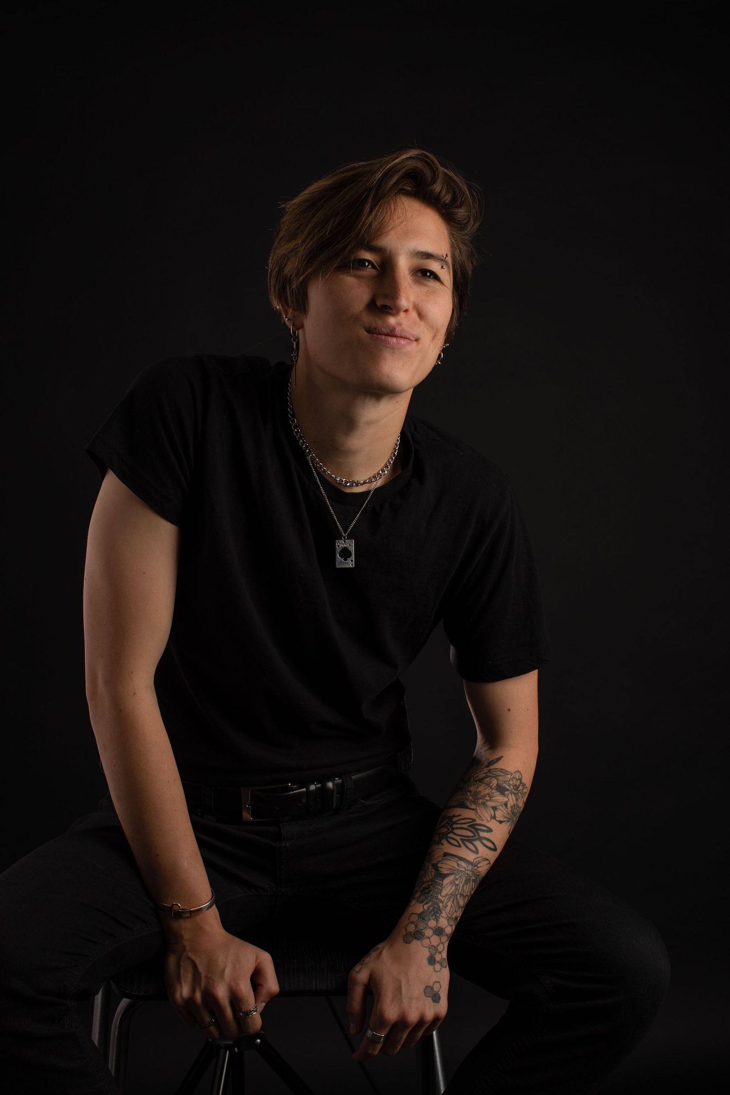 Moody studio portraits in black t-shirt showcasing casual poses and tattoo artwork.