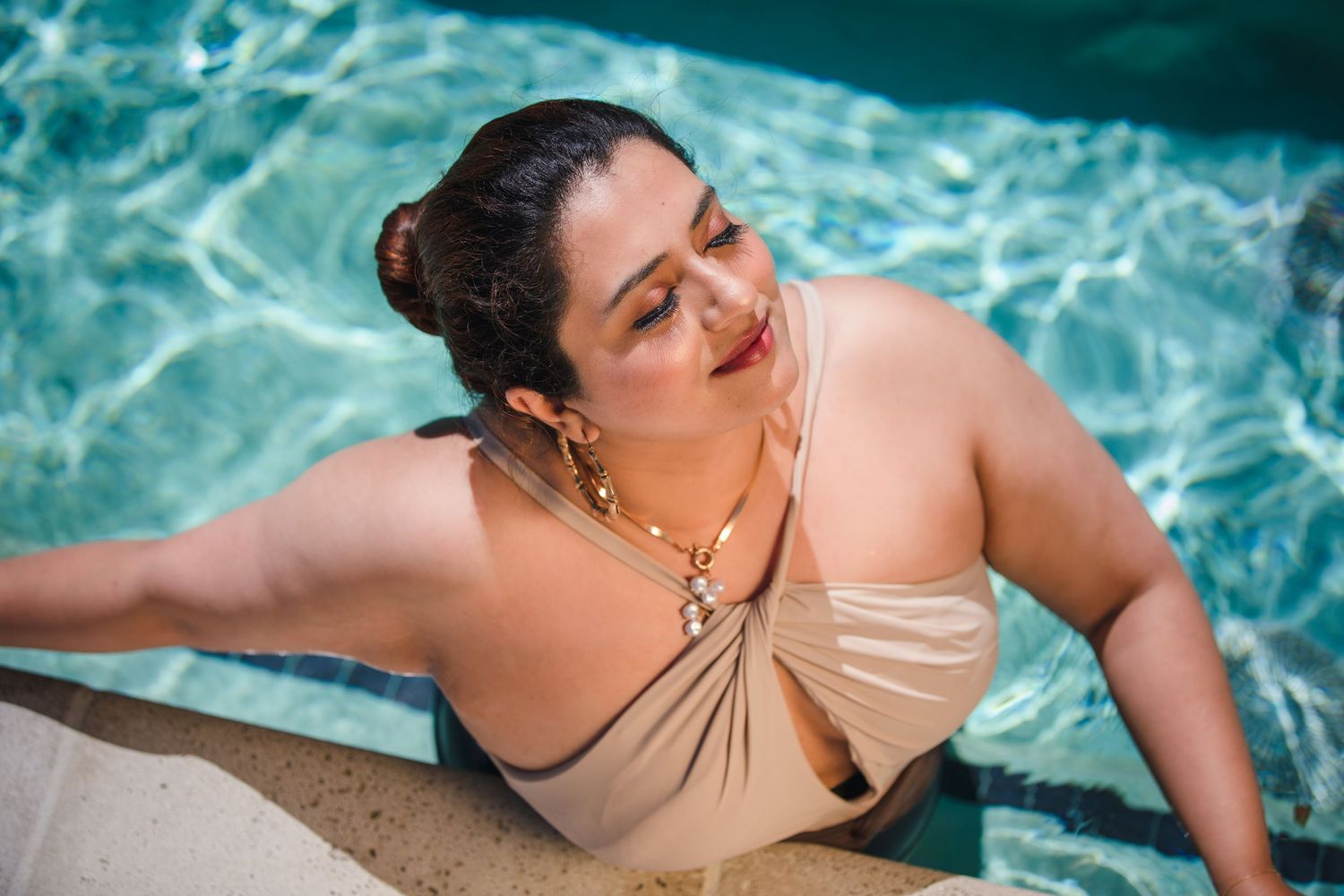 Relaxed poolside portrait with beige swimwear and gold jewelry against turquoise water.