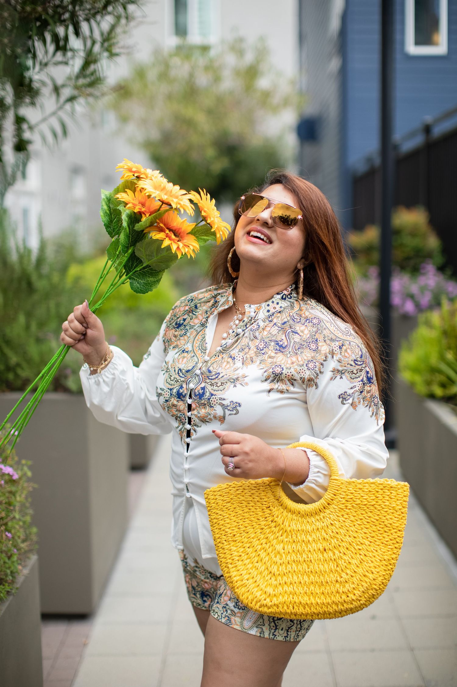 Outdoor fashion photography featuring a yellow handbag, sunflowers, and embroidered white blouse.