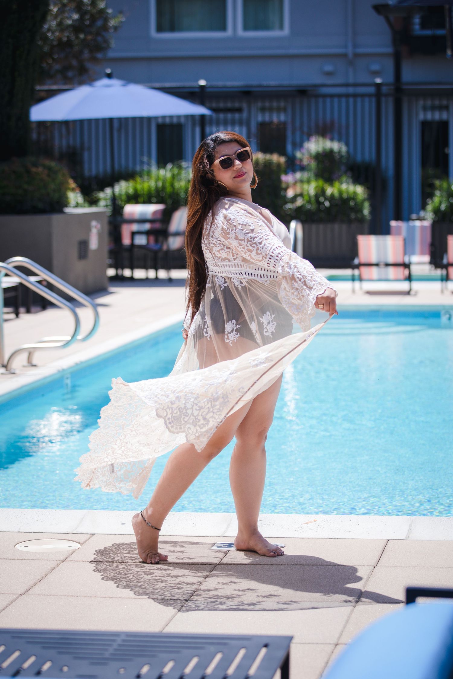 Flowing white lace coverup twirling by a swimming pool on a sunny summer day.