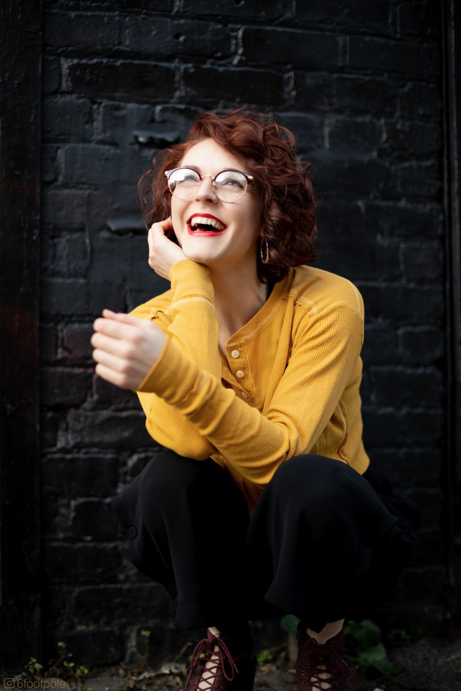 Joyful portrait in yellow sweater and glasses against dark brick wall background.
