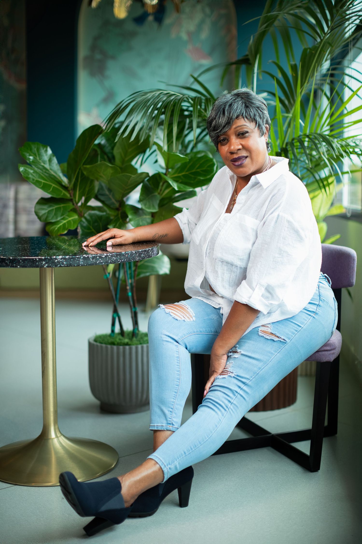 A person in light denim and heels reclines on a chair in a modern setting.