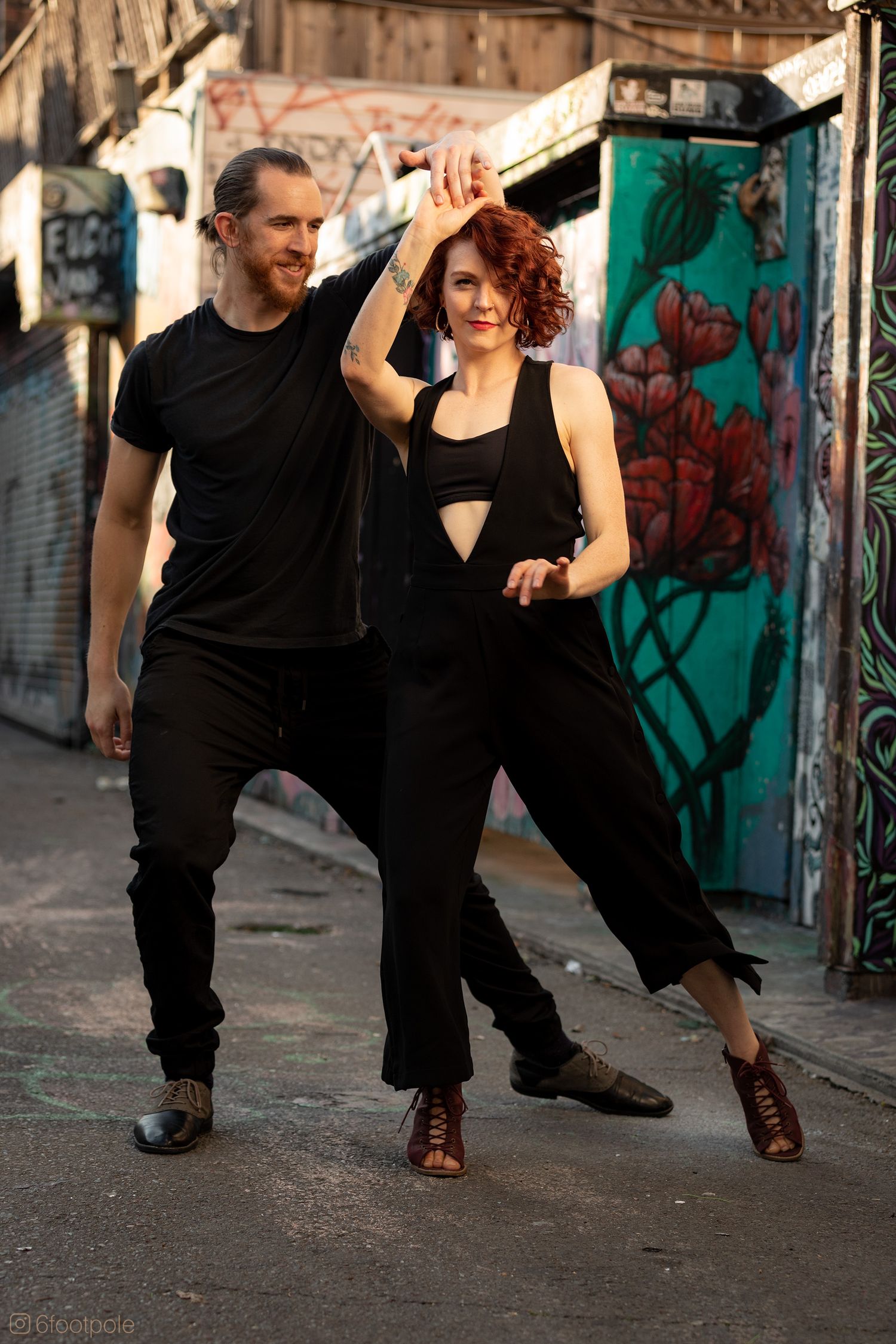 Dance performers in black outfits practicing moves in front of graffiti-covered wall.