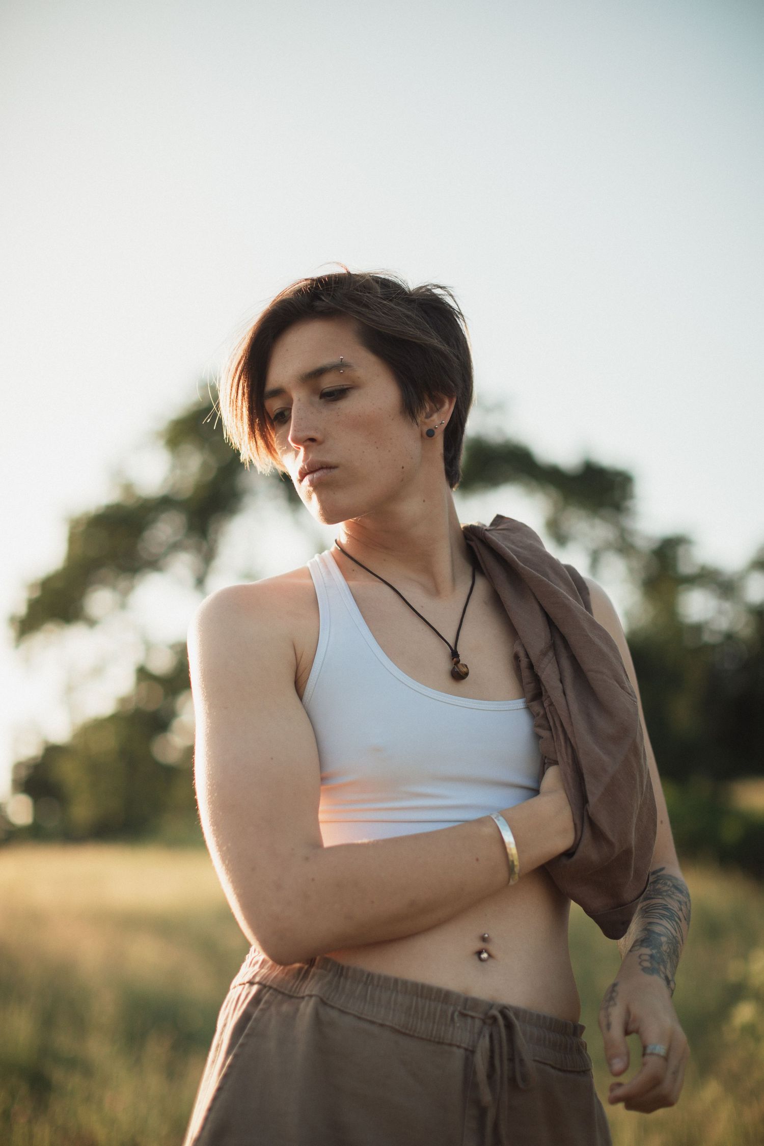 Person in white tank top and brown pants poses in golden hour sunlight.