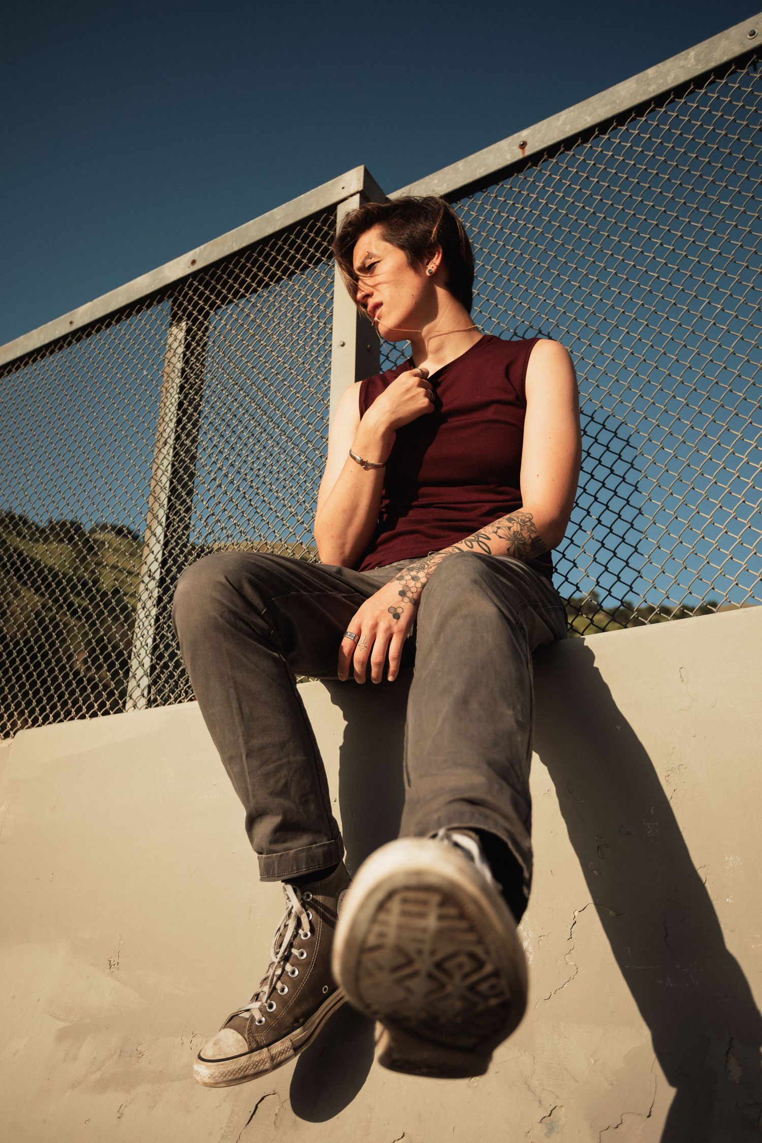 Person in casual attire sits on concrete ledge with legs extended against chain link fence.