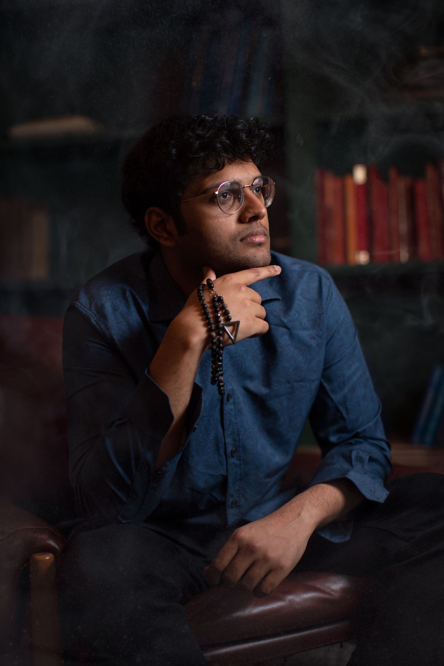 Figure in blue shirt sits thoughtfully in dark room with moody lighting.